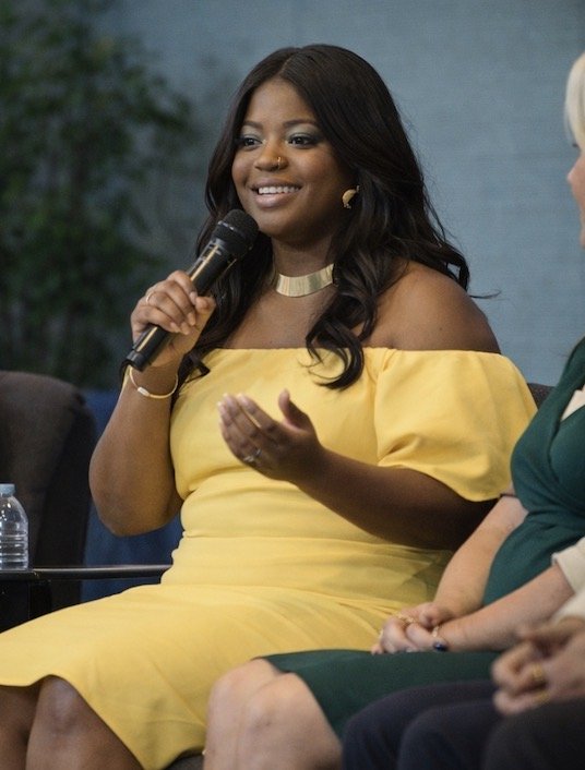 Woman in yellow dress speaking into a microphone at an event