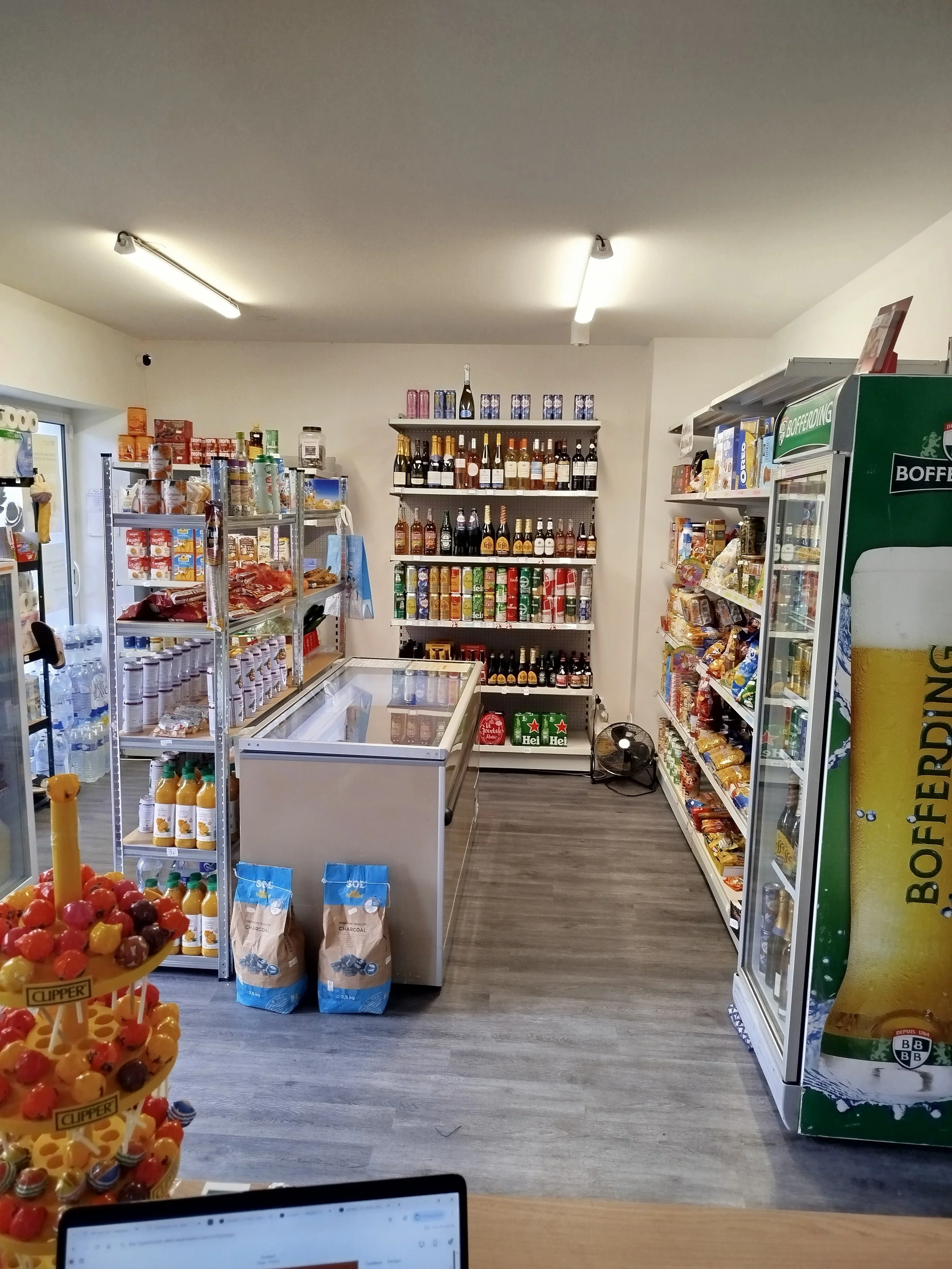 Intérieur d'un petit magasin avec étagères remplies de produits alimentaires, une glacière et une grande bouteille de bière en vitrine