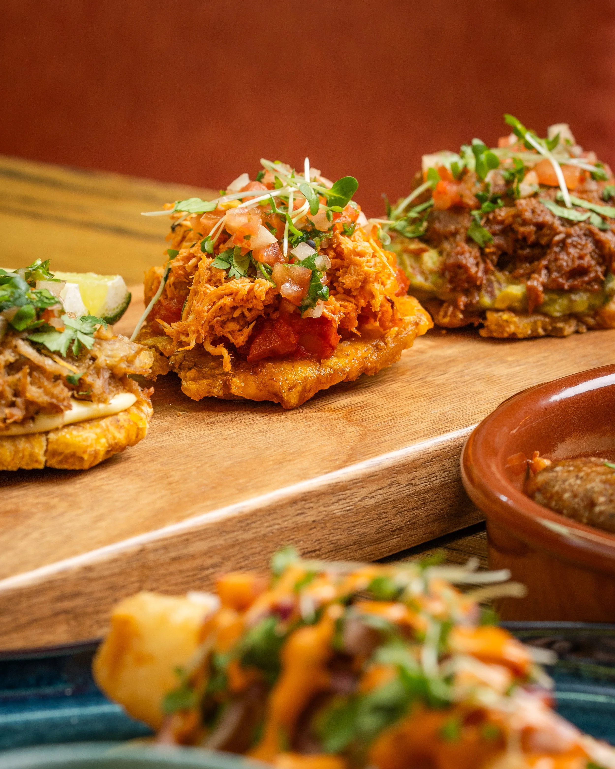 Three various Mexican tostadas topped with shredded meat, guacamole, fresh herbs, and salsa, displayed on a wooden serving board.