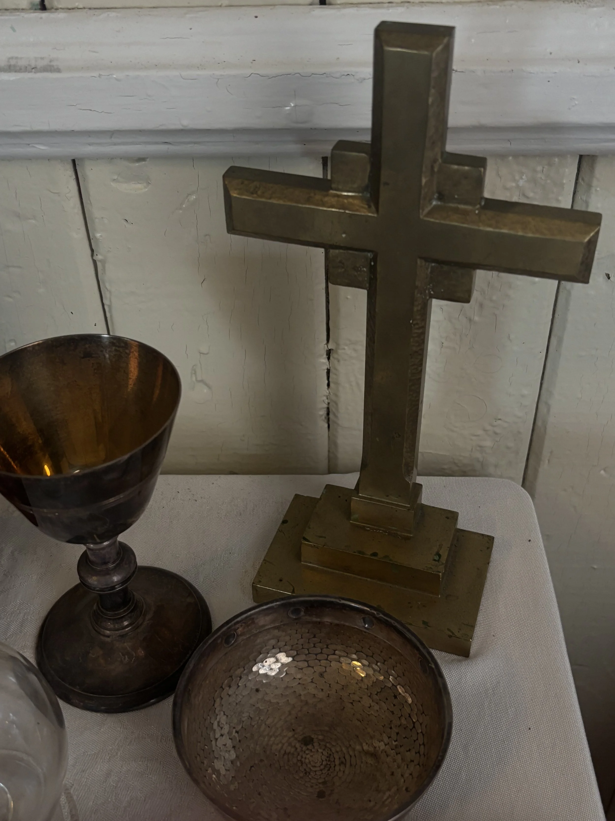 A brass cross statue and two bowls on a white tablecloth, with a white wooden wall in the background.