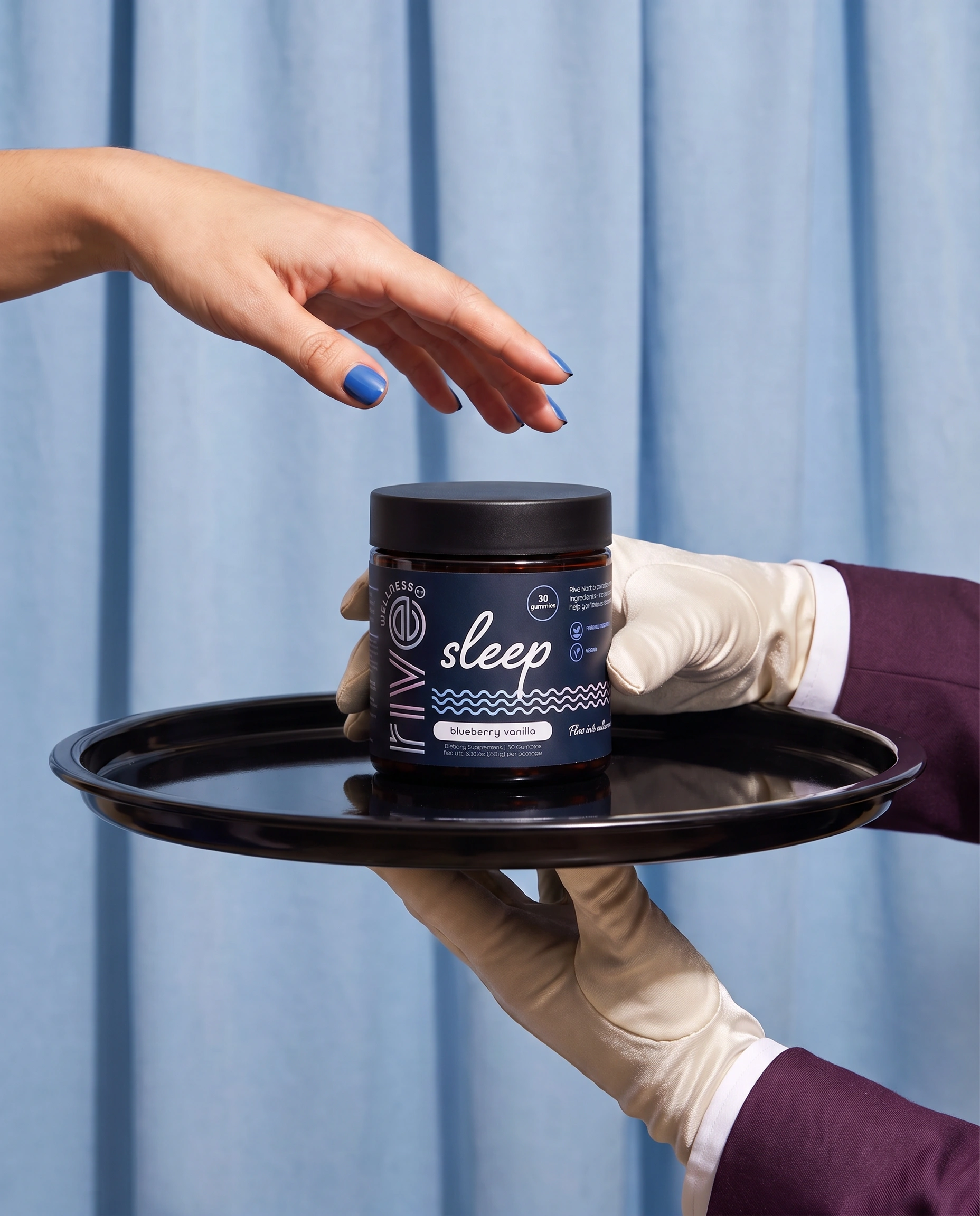 A person wearing a beige glove holding a black tray with a small jar of HyperSleep blueberry vanilla gummies against a blue curtain background.