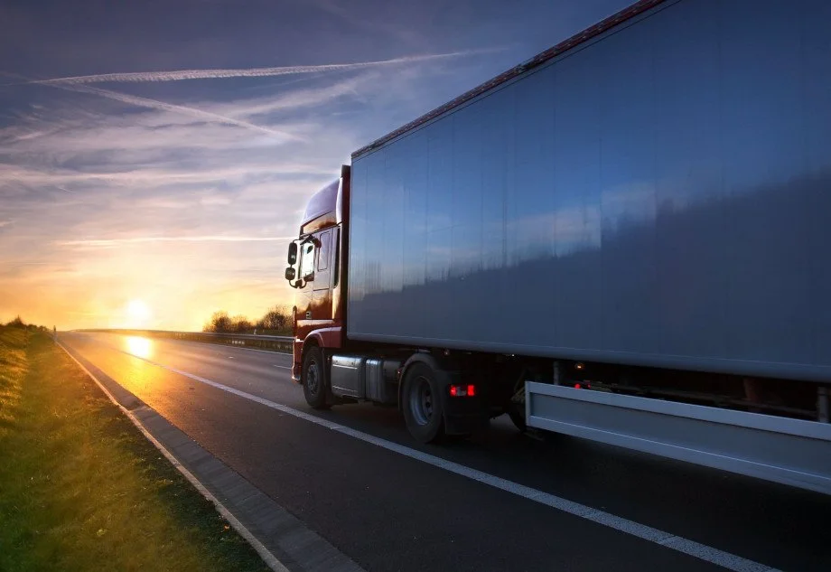 A semi-truck driving on a highway at sunset.