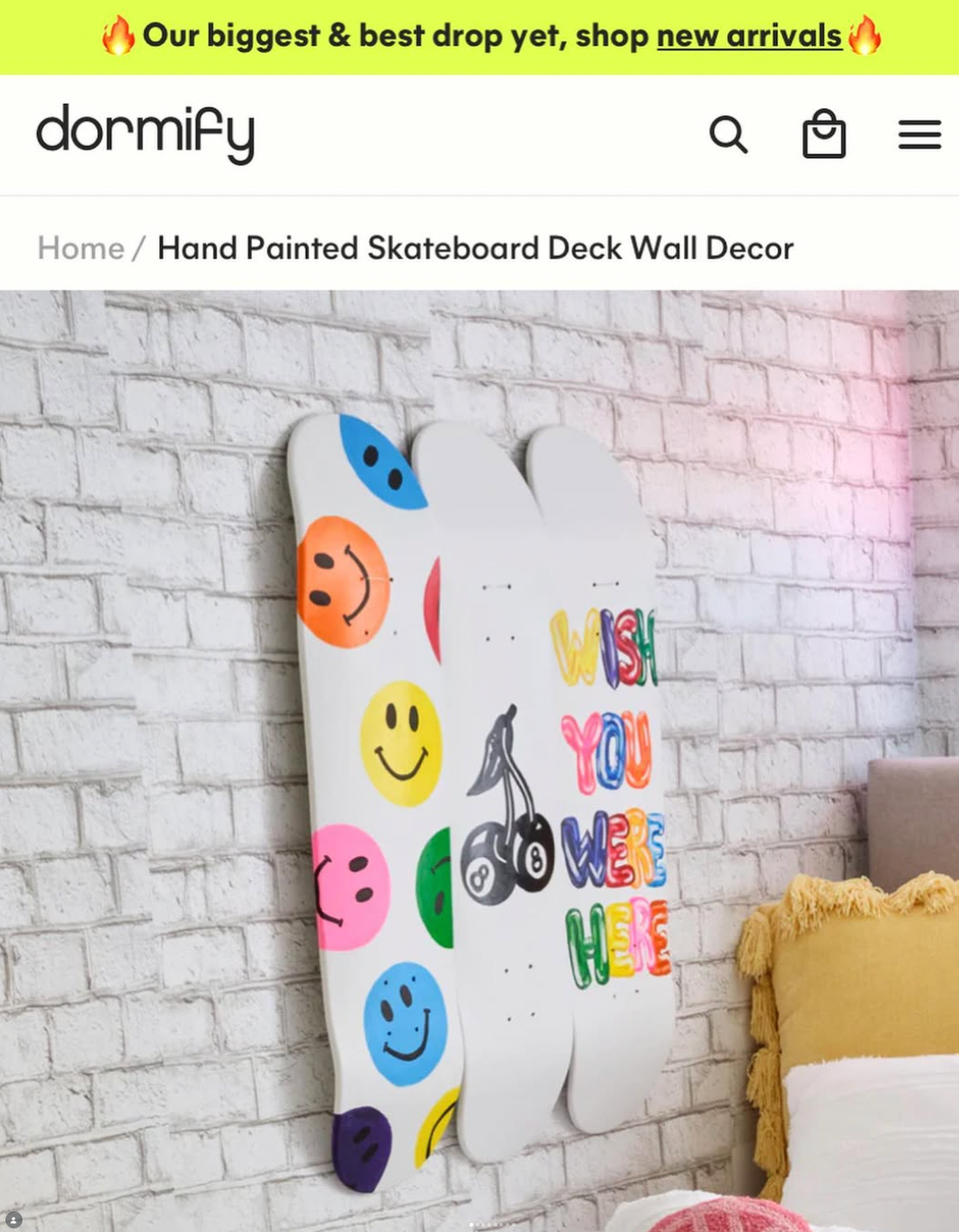 Hand-painted skateboard deck wall decor with colorful smiley faces, a cherry, and the words "Wish You Were Here" on a white brick wall background.
