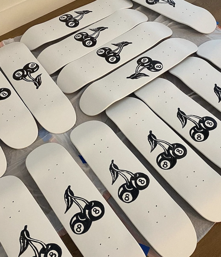 Multiple white skateboard decks with a black and white logo of two stacked billiard balls with a stylized leaf or wing extending from the top ball.