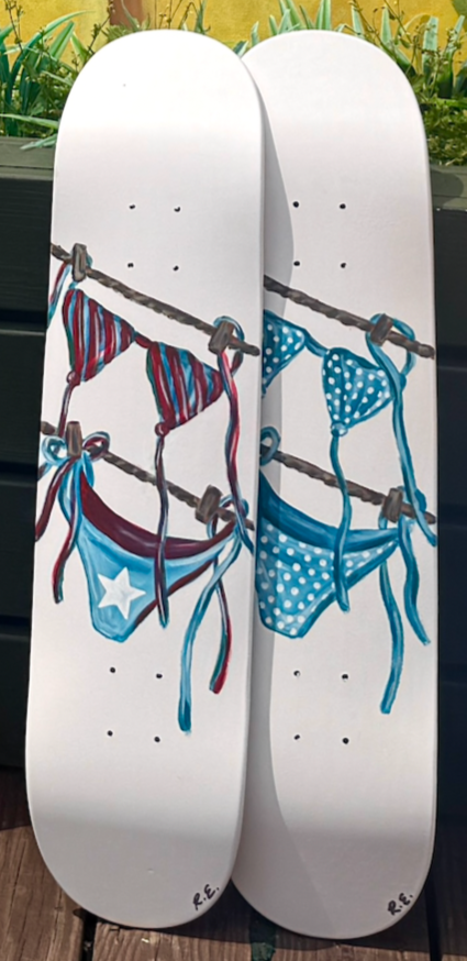 Two skateboards with painted swimsuits hanging on a clothesline, depicted in a whimsical style.