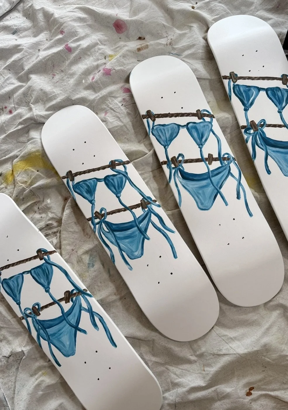 Four skateboard decks painted with blue bikini tops and bottoms hanging on a clothesline.