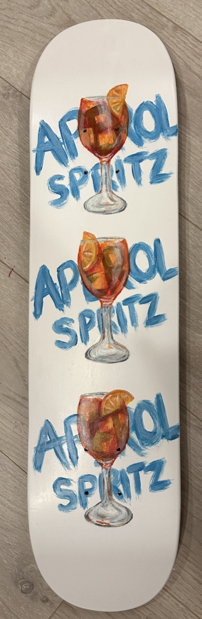 A skateboard with a designed image of three Aperol Spritz drinks, each with orange slices on the rim, and the words 'Aperol Spritz' written in blue letters.