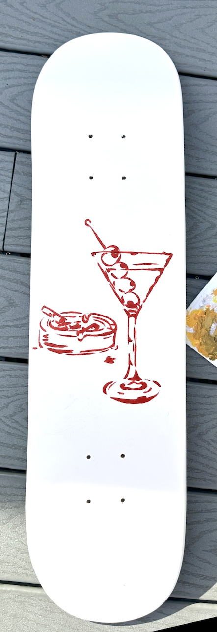 White skateboard deck with a red line drawing of a cocktail glass with cherries and a small dessert with a spoon next to it.