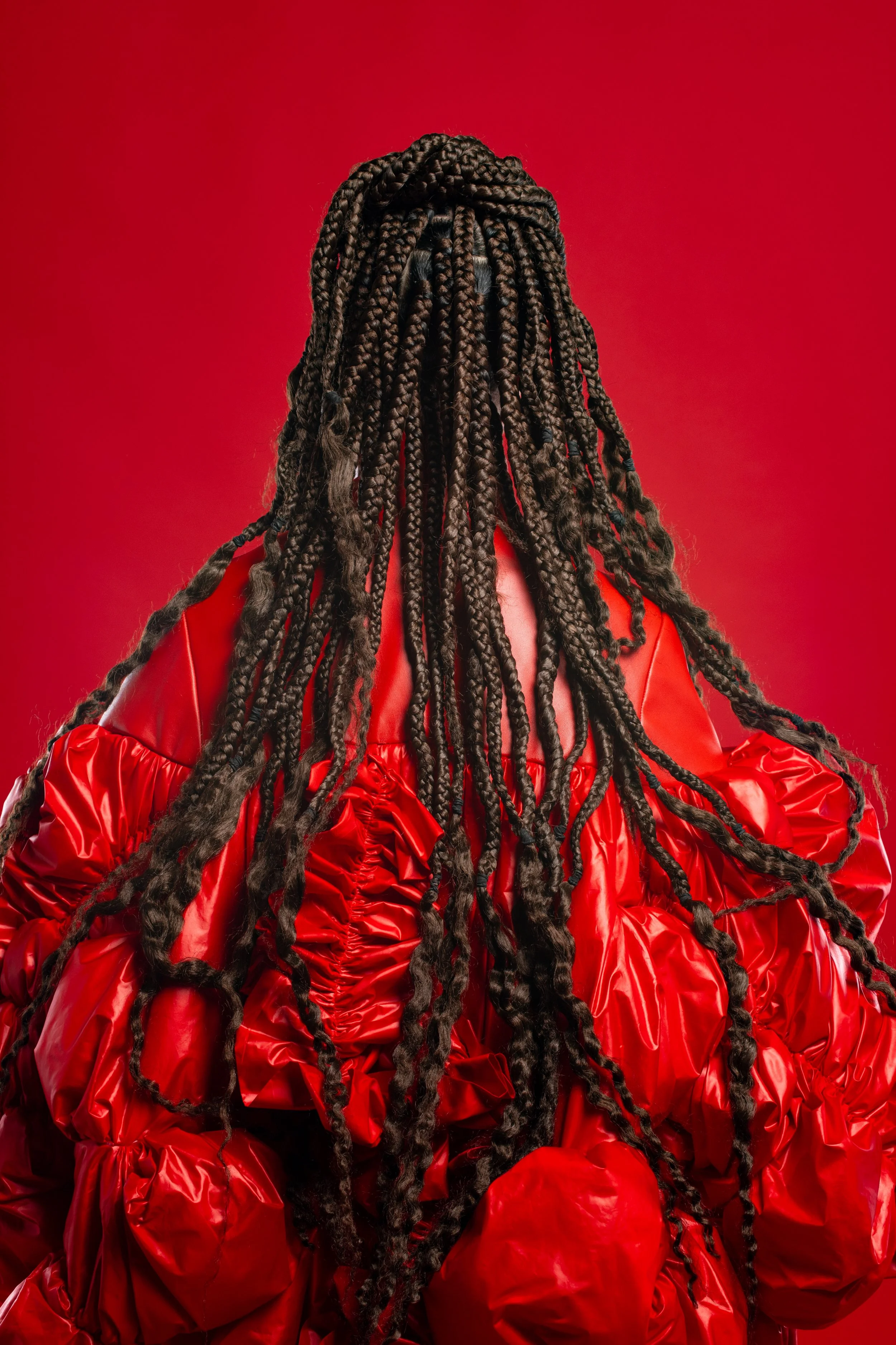 Persona con cabello trenzado y larga, vestida con un abrigo rojo brillante, de espaldas en fondo rojo