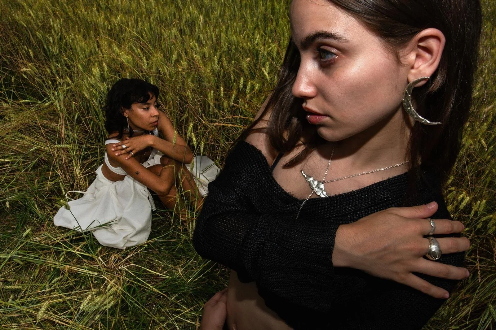 Dos mujeres con accesorios de plata en un campo de hierba, una en primer plano y otra en el fondo