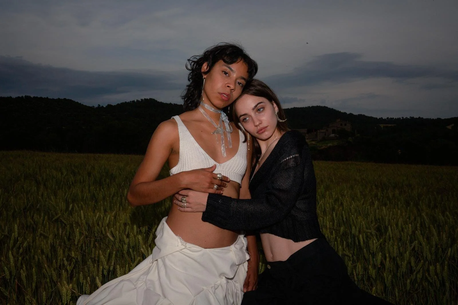Dos mujeres con ropa moderna en un campo, bajo un cielo nublado.