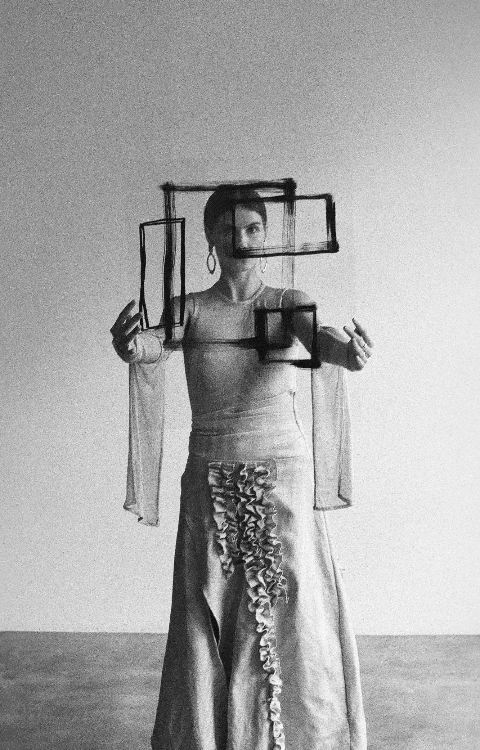 Mujer artísticamente posando frente a una pared, dibujando formas con un rotulador sobre una superficie de vidrio o plexiglás