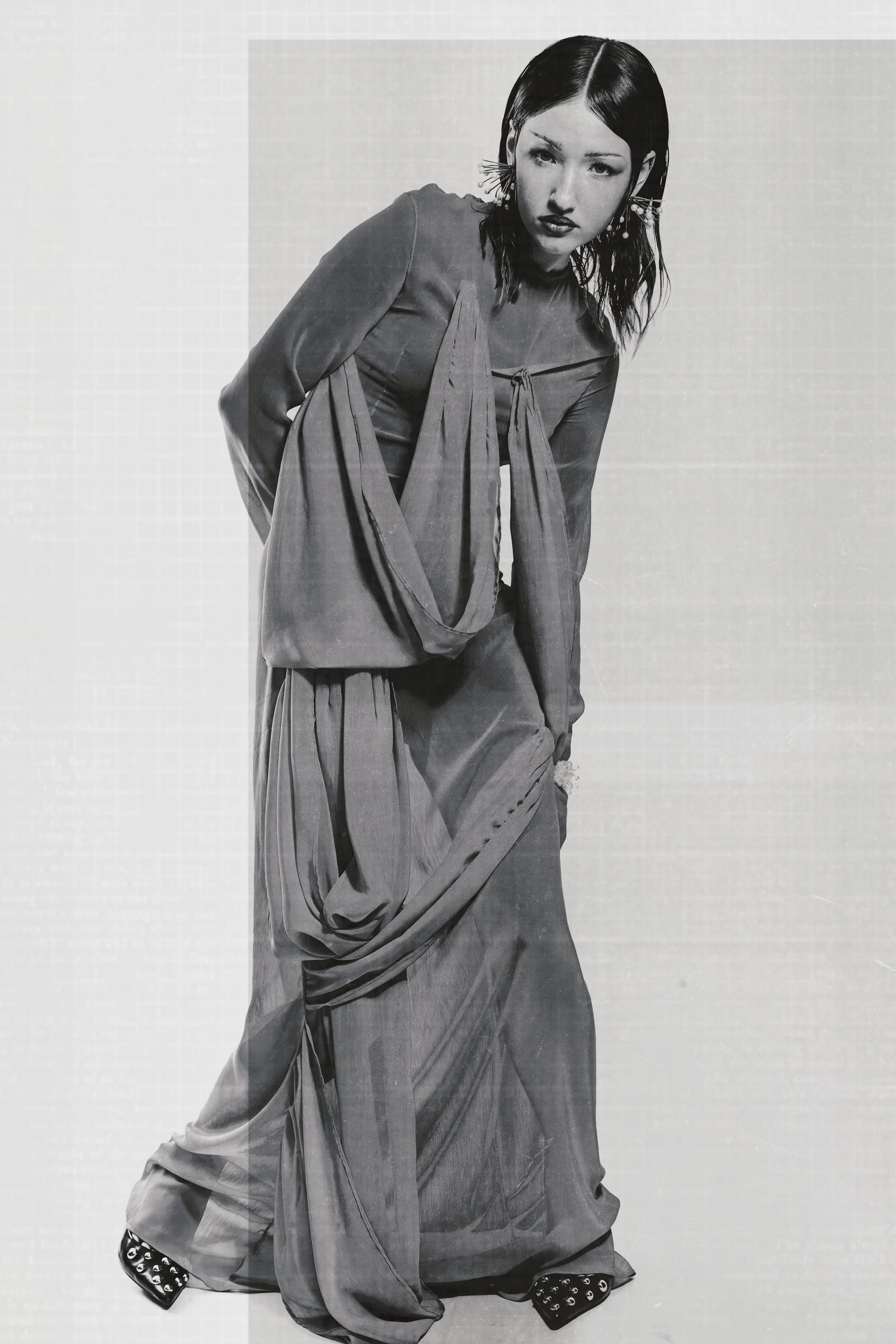 Retrato en blanco y negro de una mujer joven vestida con ropa de moda, posando con expresión seria y cabello liso y oscuro.