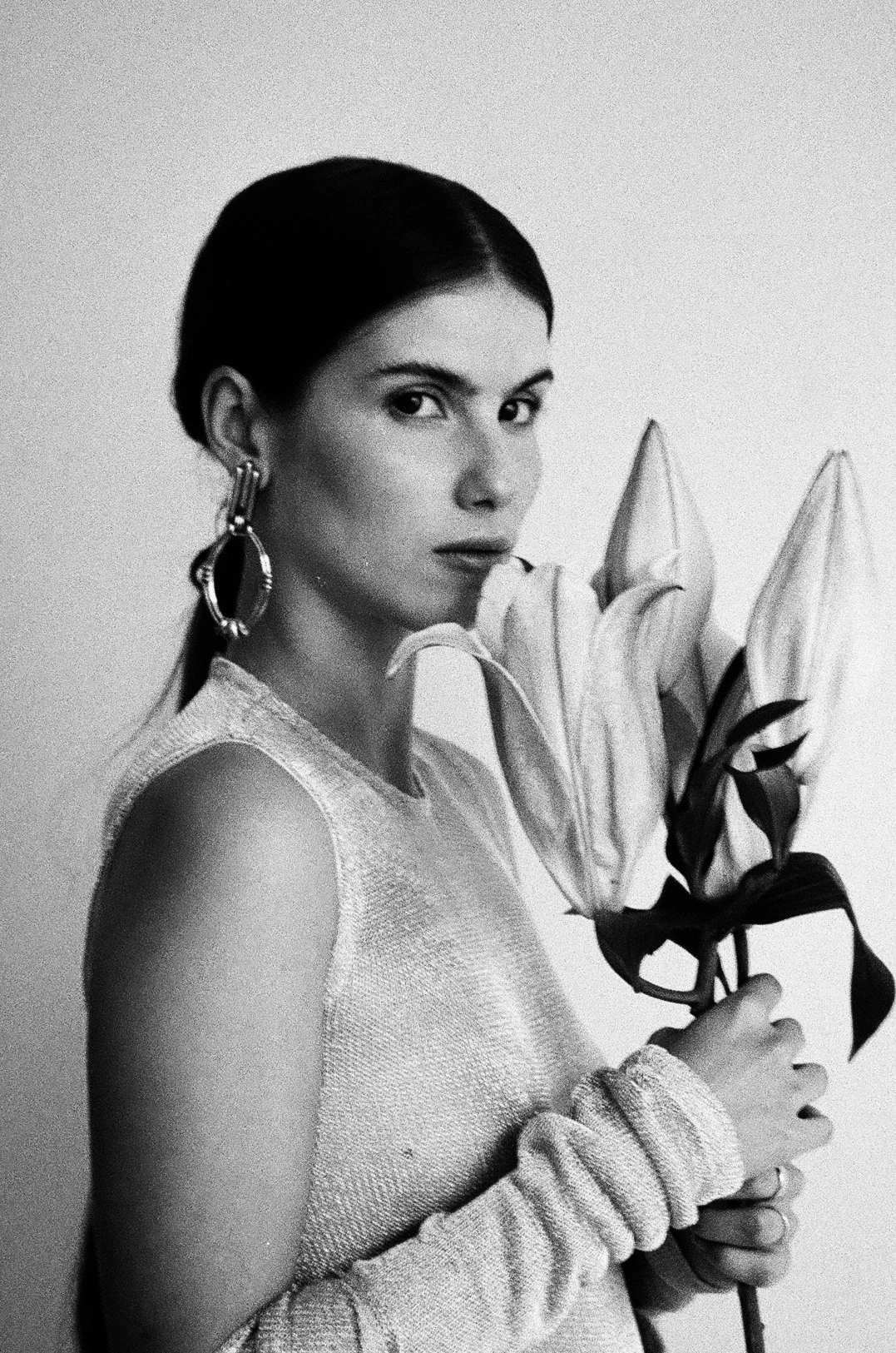 Una mujer sosteniendo un ramo de lirios, vestida con ropa brillante y usando aretes grandes.