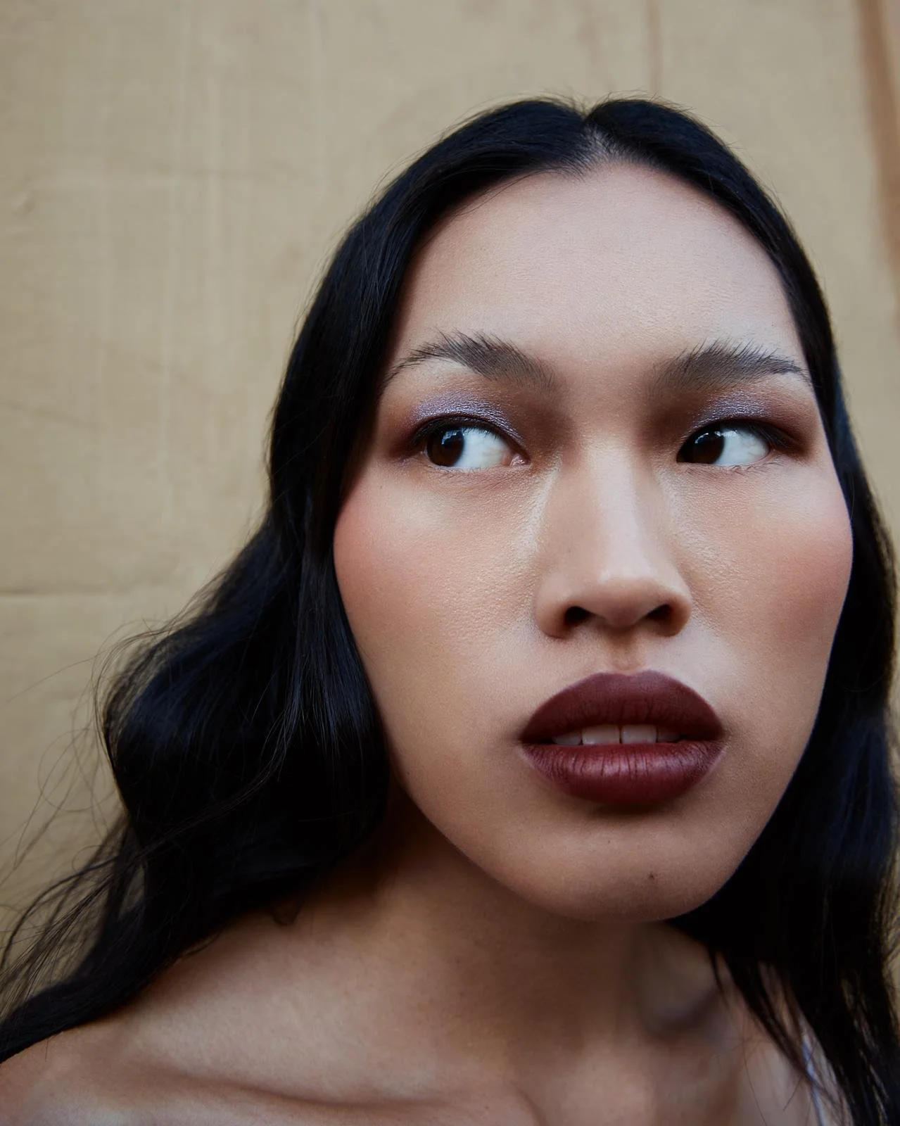 Primer plano de rostro de mujer con piel clara, labios oscuros y ojos oscuros, fondo beige.