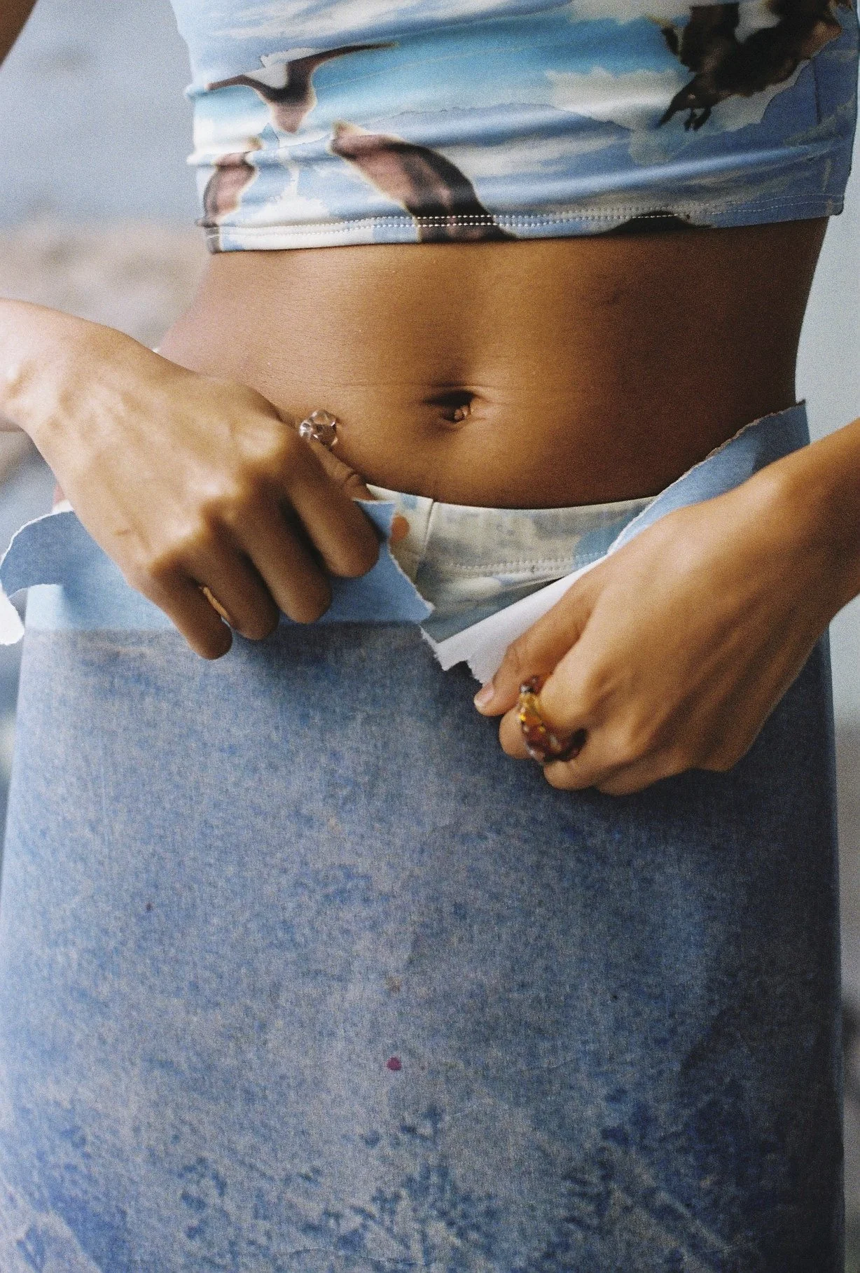 Primer plano de una mujer ajustándose la ropa, mostrando su abdomen desnudo y usando accesorios en las manos.