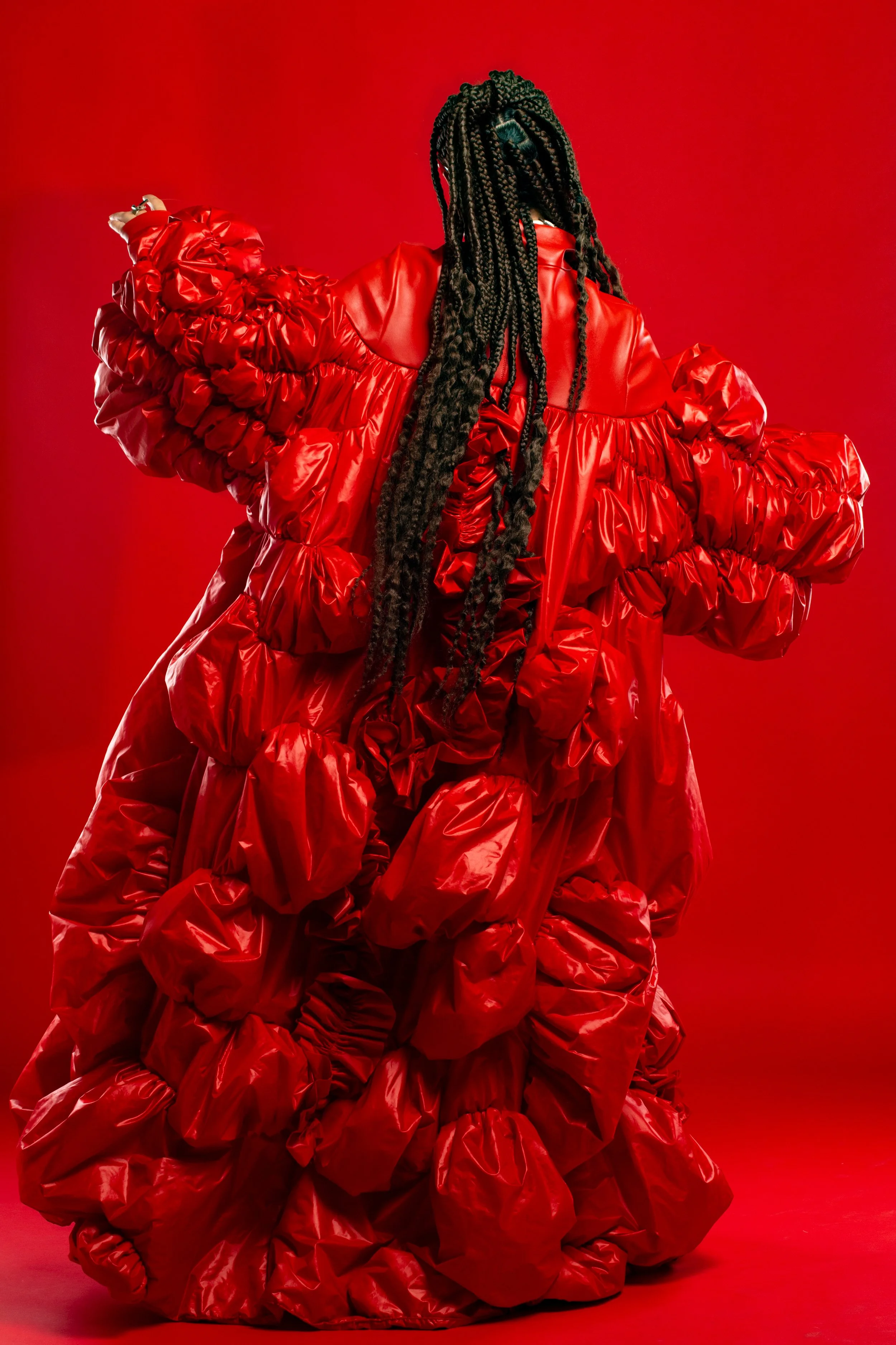 Una persona de espaldas con un vestido llamativo de color rojo, con telas y volantes gruesos, sobre un fondo rojo.