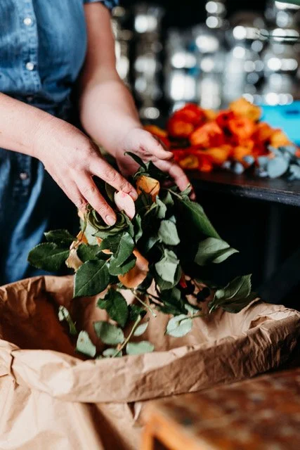 Person holding a bunch of orange roses over a paper-lined container