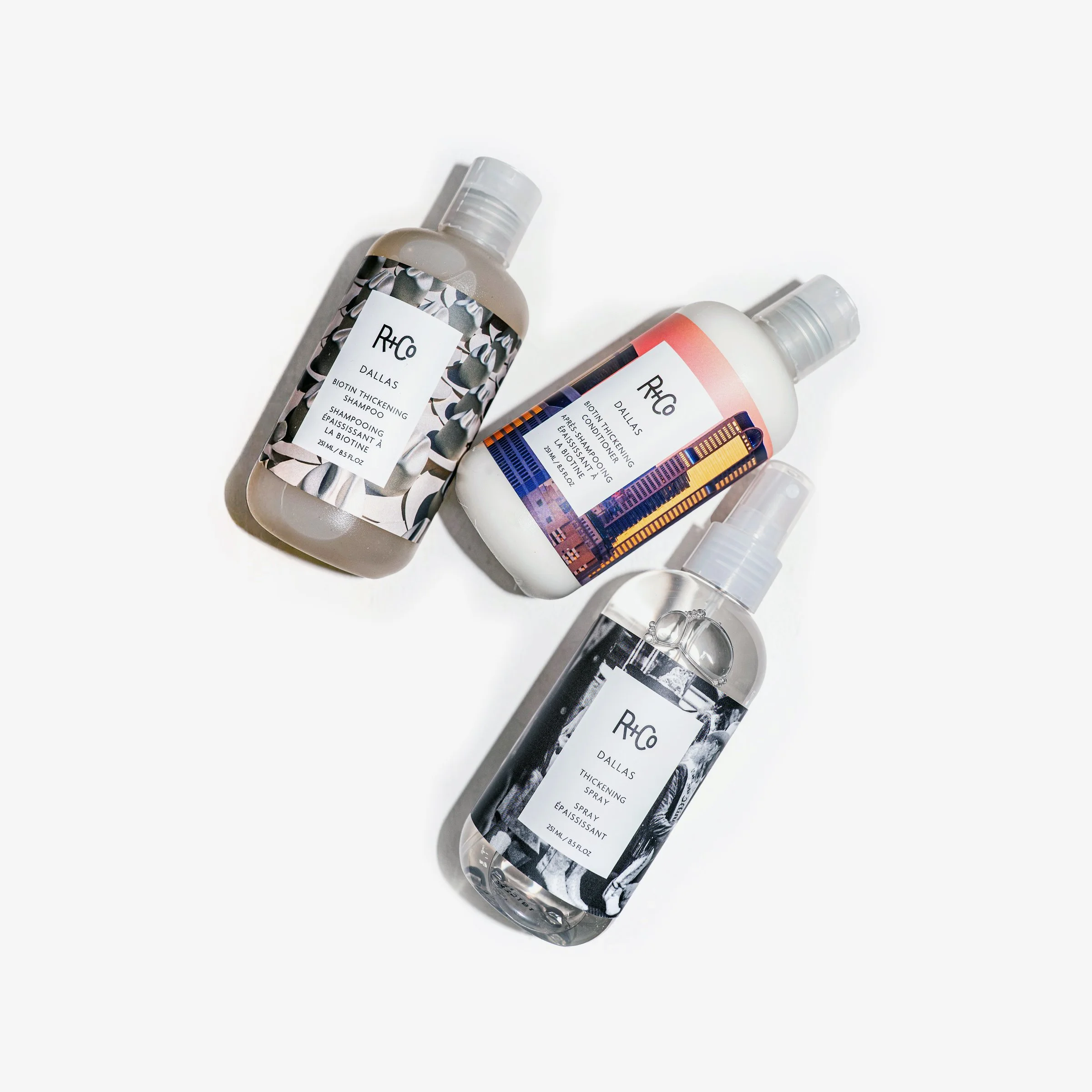 Three Rexco Dallas beauty products with patterned labels on a white background, including a thickening shampoo, a thickening spray, and an intensive conditioning spray.
