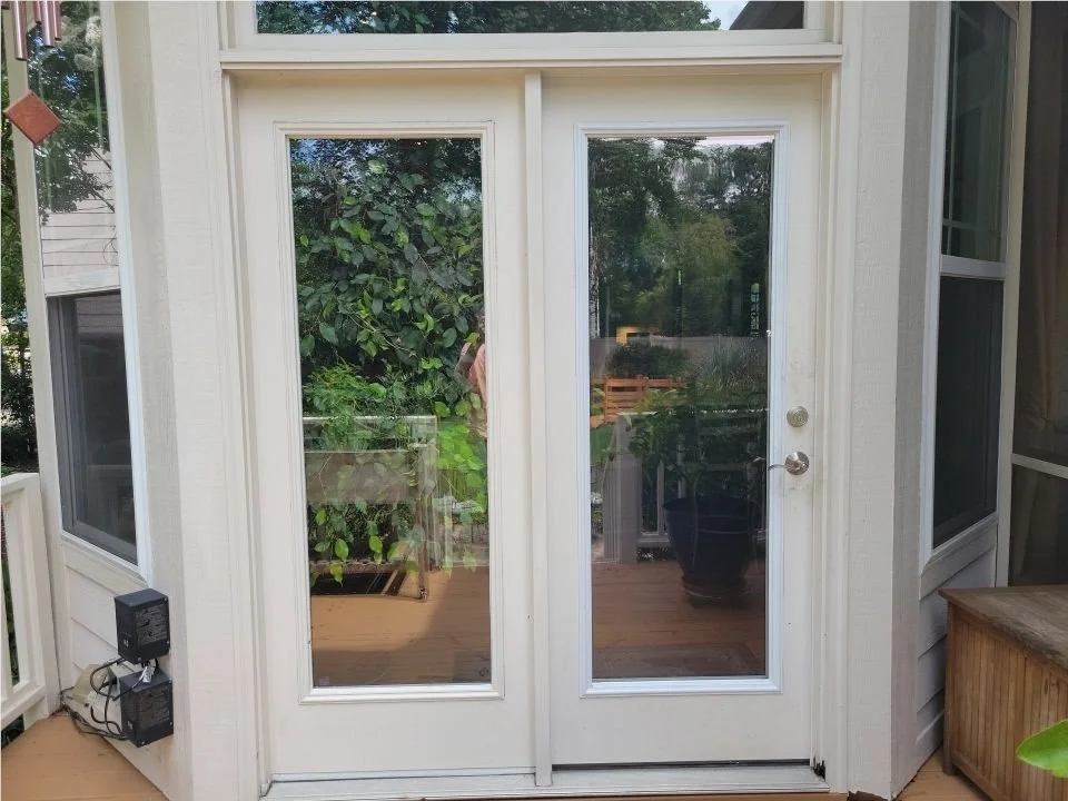 A pair of white-framed sliding glass doors leading to an outdoor deck, with reflections of trees and sky visible in the glass.