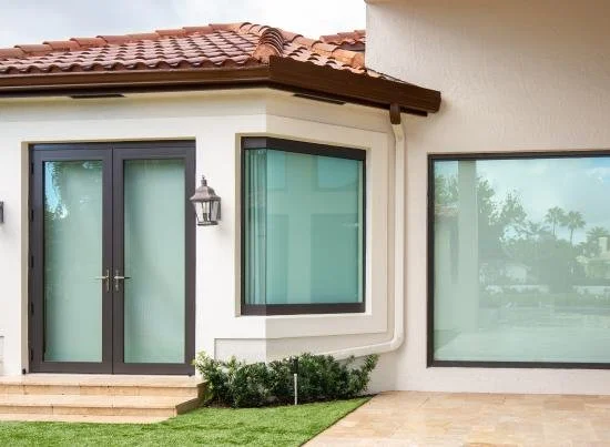Exterior view of a house with glass sliding doors, a large window, a mail lantern, and a small garden with green grass and shrubs.