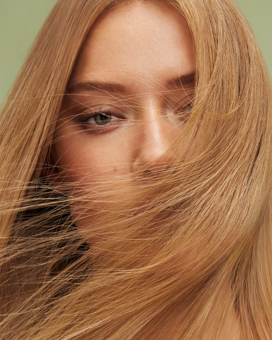 Close-up of a woman with long, flowing blonde hair partially covering her face, with one eye visible.