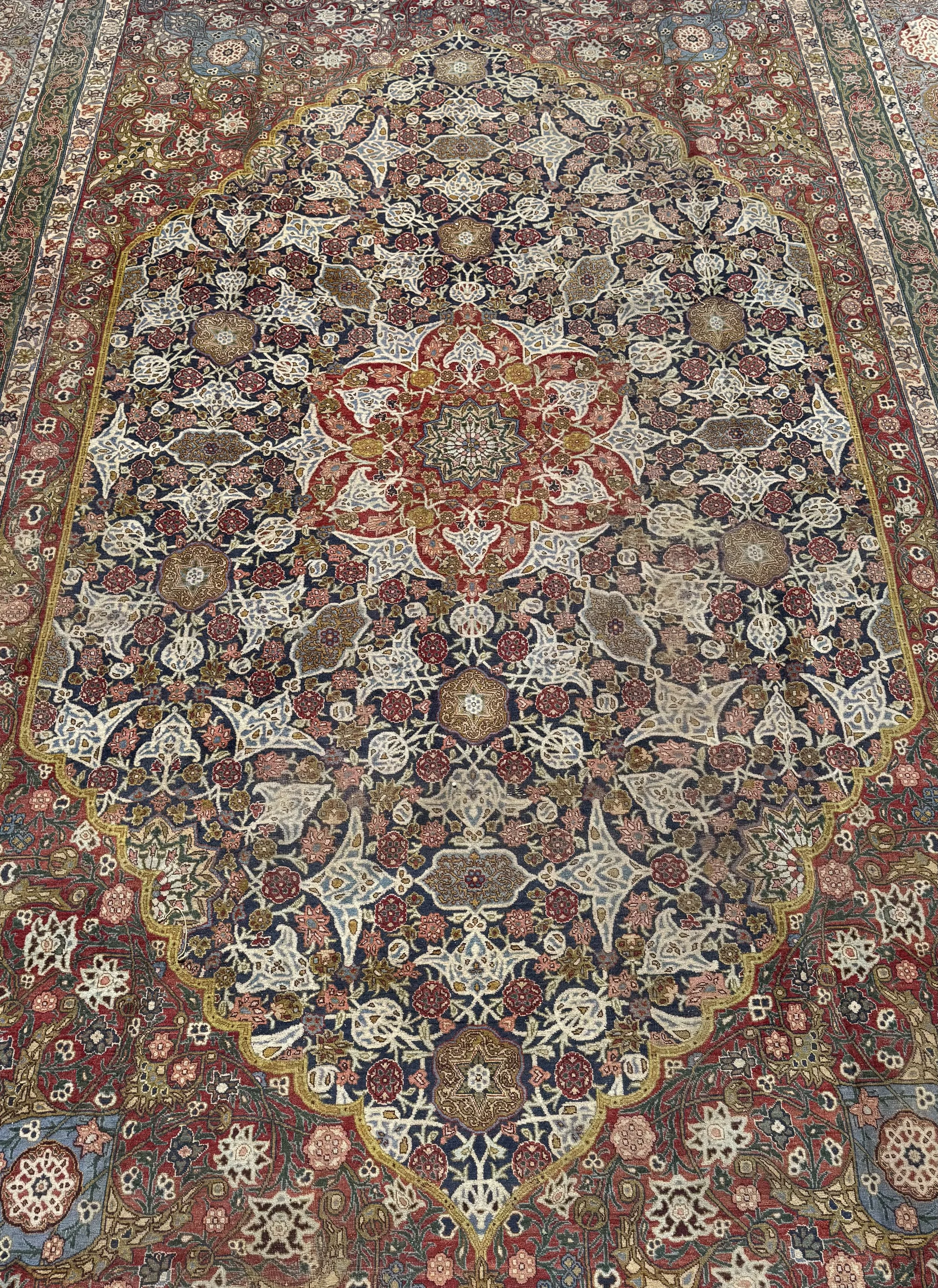 A detailed Persian-style rug with a central floral medallion, surrounded by intricate geometric and floral patterns in red, navy, cream, brown, and green colors.