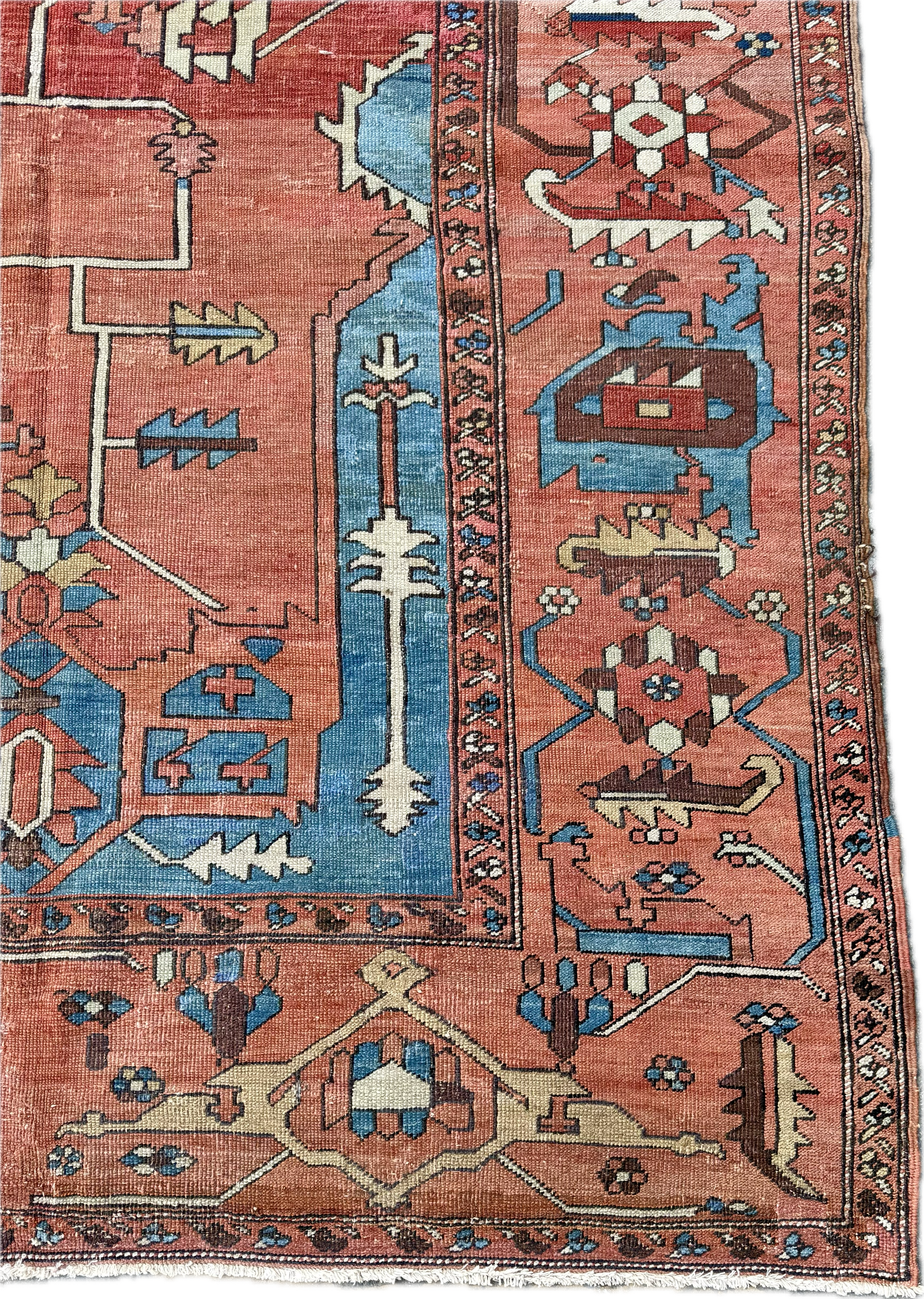 Close-up of a traditional woven rug with intricate geometric patterns in shades of red, blue, cream, and brown, featuring borders and central motifs.
