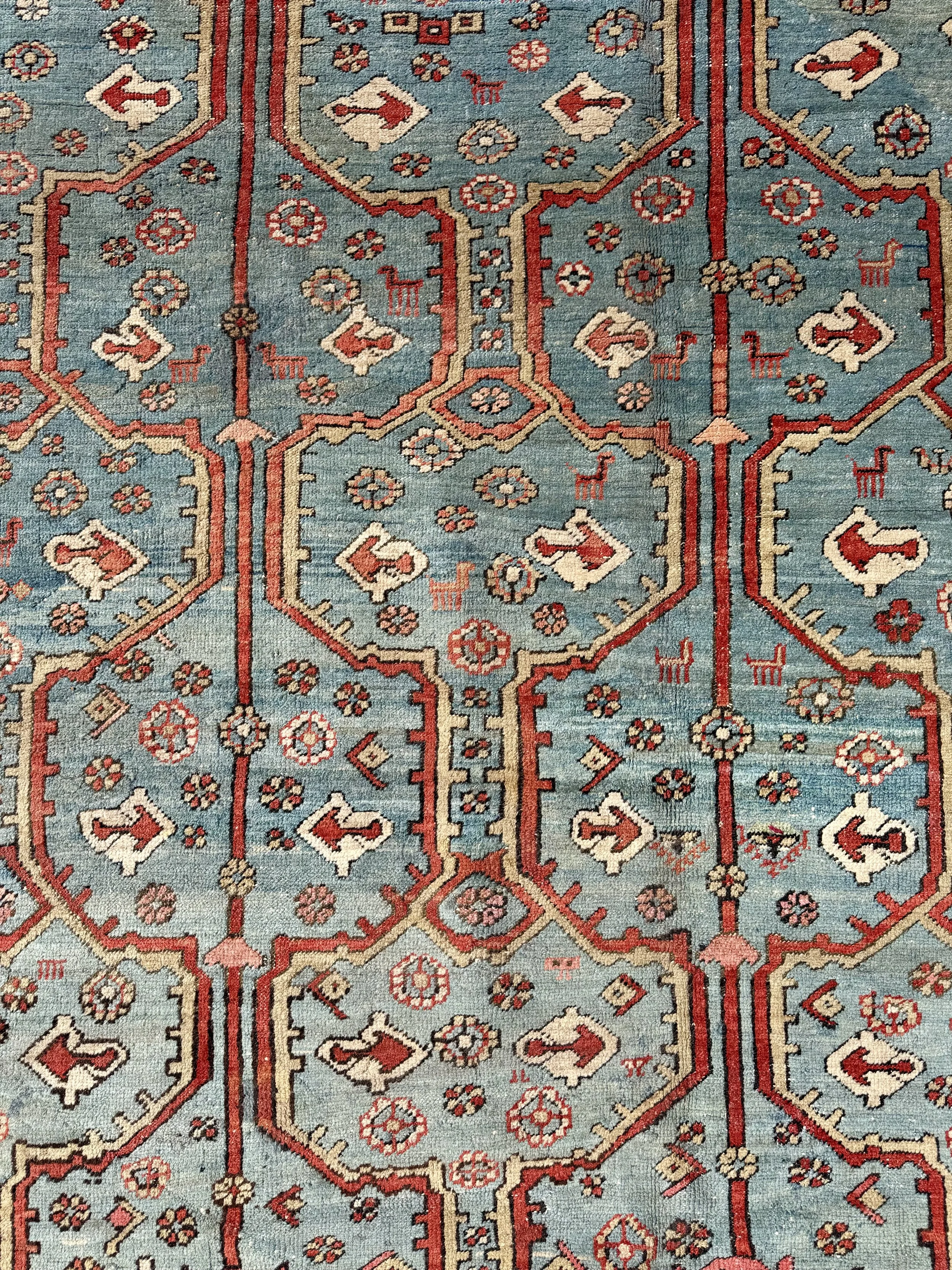 Close-up of a traditional patterned rug with geometric shapes, floral motifs, and animal figures in red, cream, and blue colors.