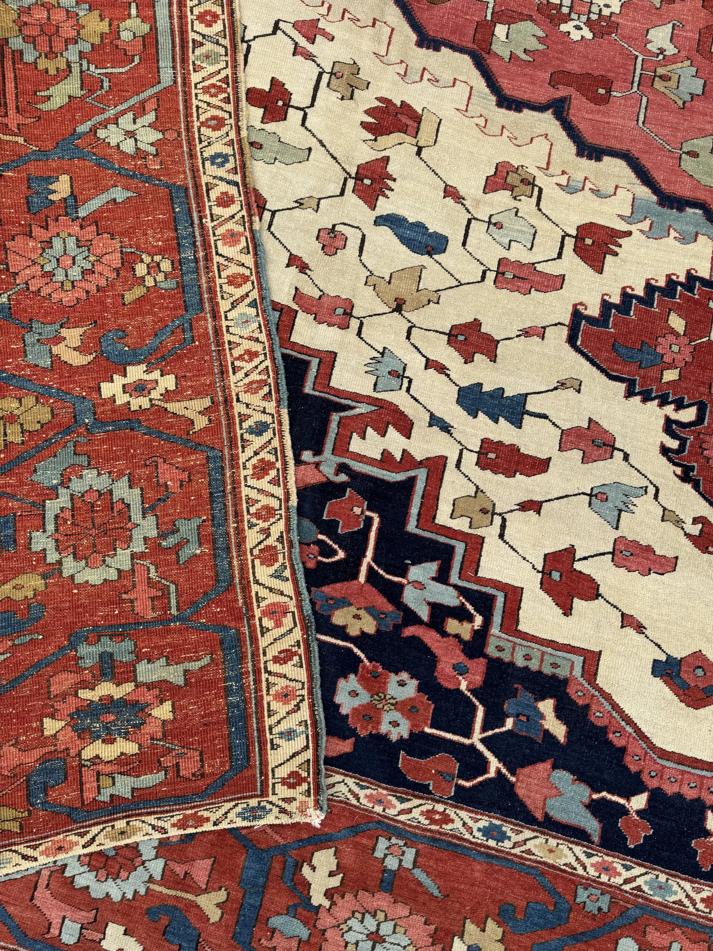 Close-up of a traditional patterned area rug with red, beige, blue, and green colors, featuring floral and geometric designs.