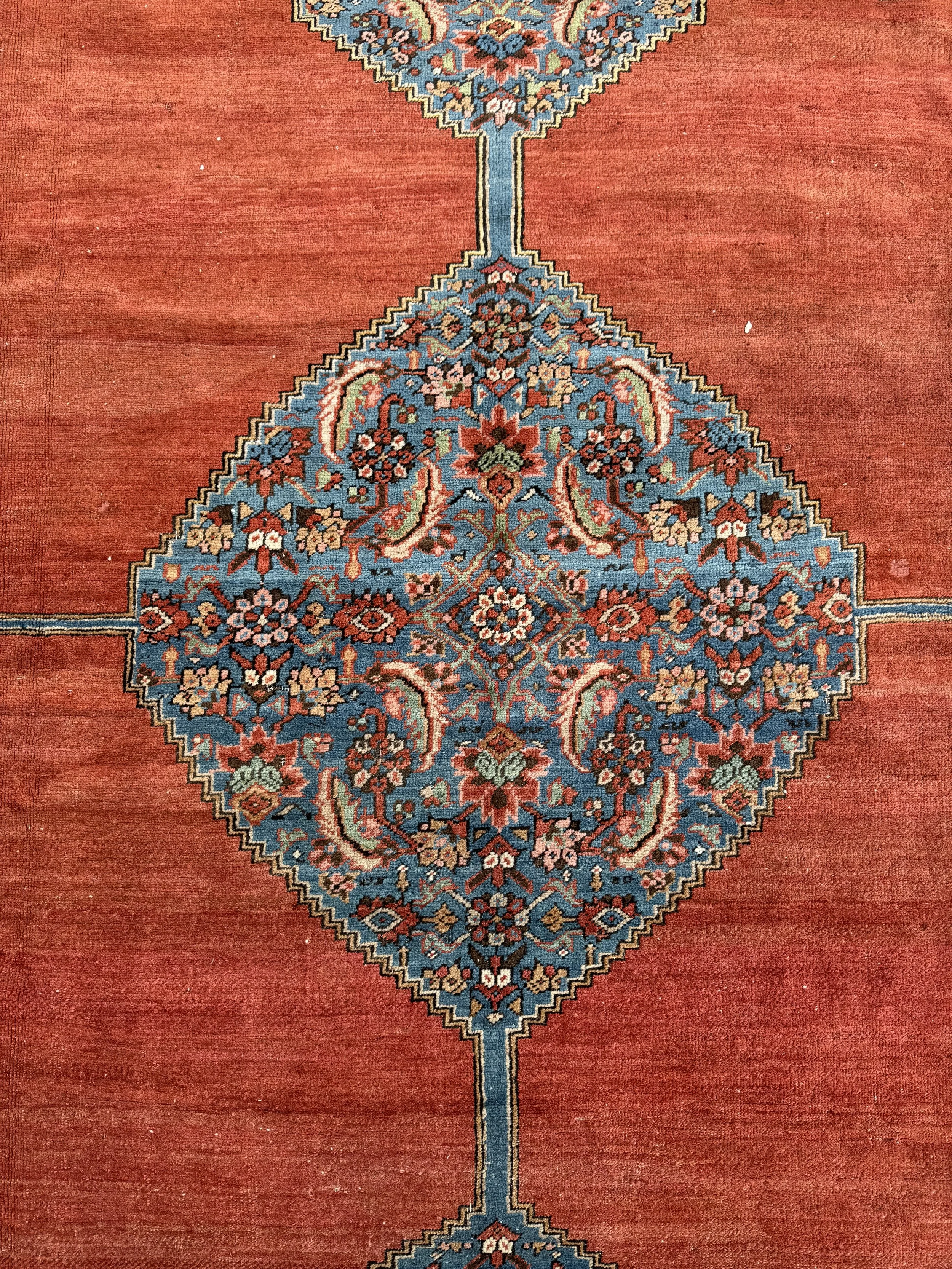 A traditional oriental rug with a central medallion pattern featuring floral motifs in shades of red, blue, beige, and green. The rug has a red background and intricate geometric borders.
