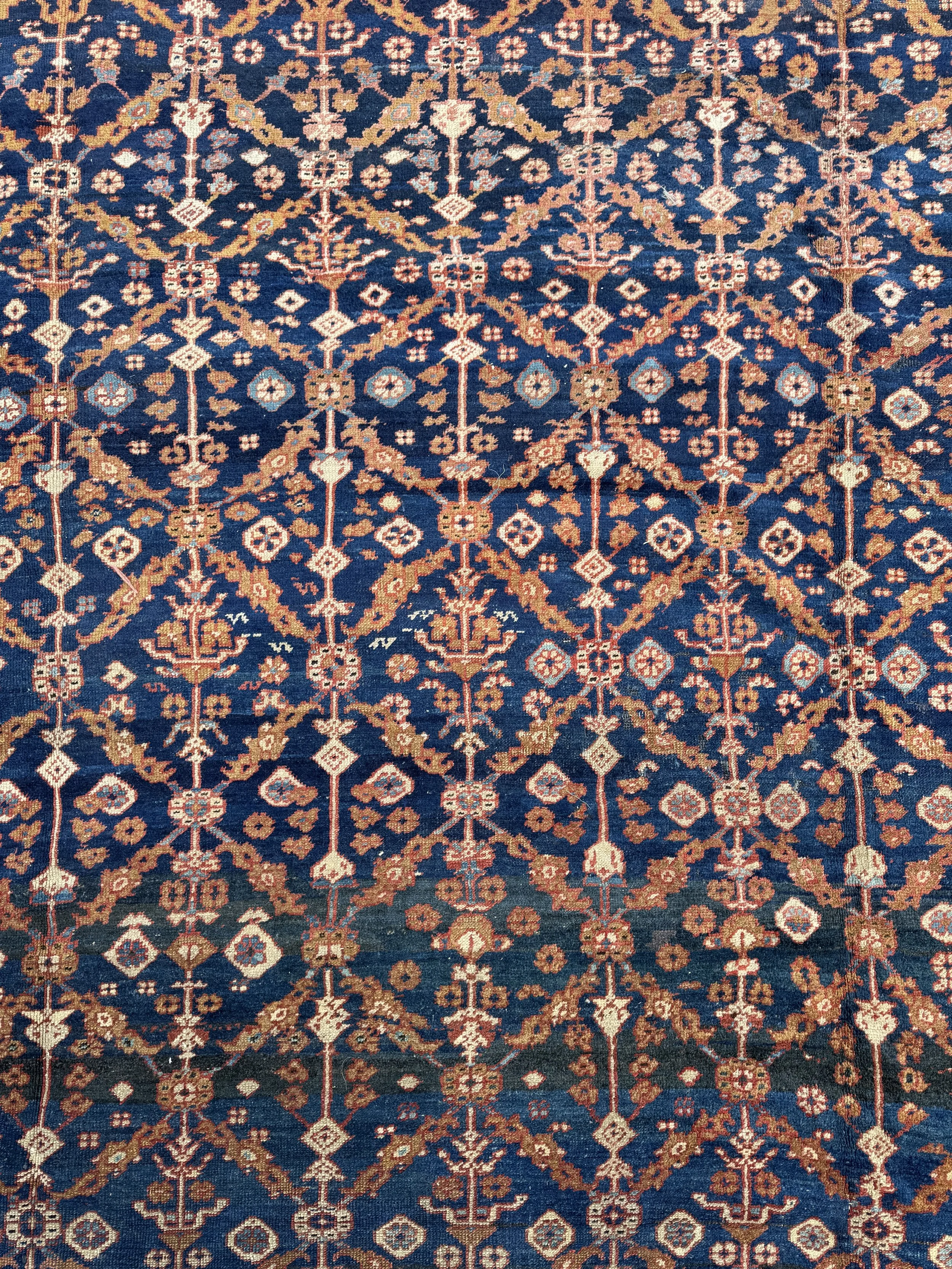 Close-up of a traditional Persian-style patterned rug with intricate geometric floral designs in beige, brown, and light blue on a dark blue background.