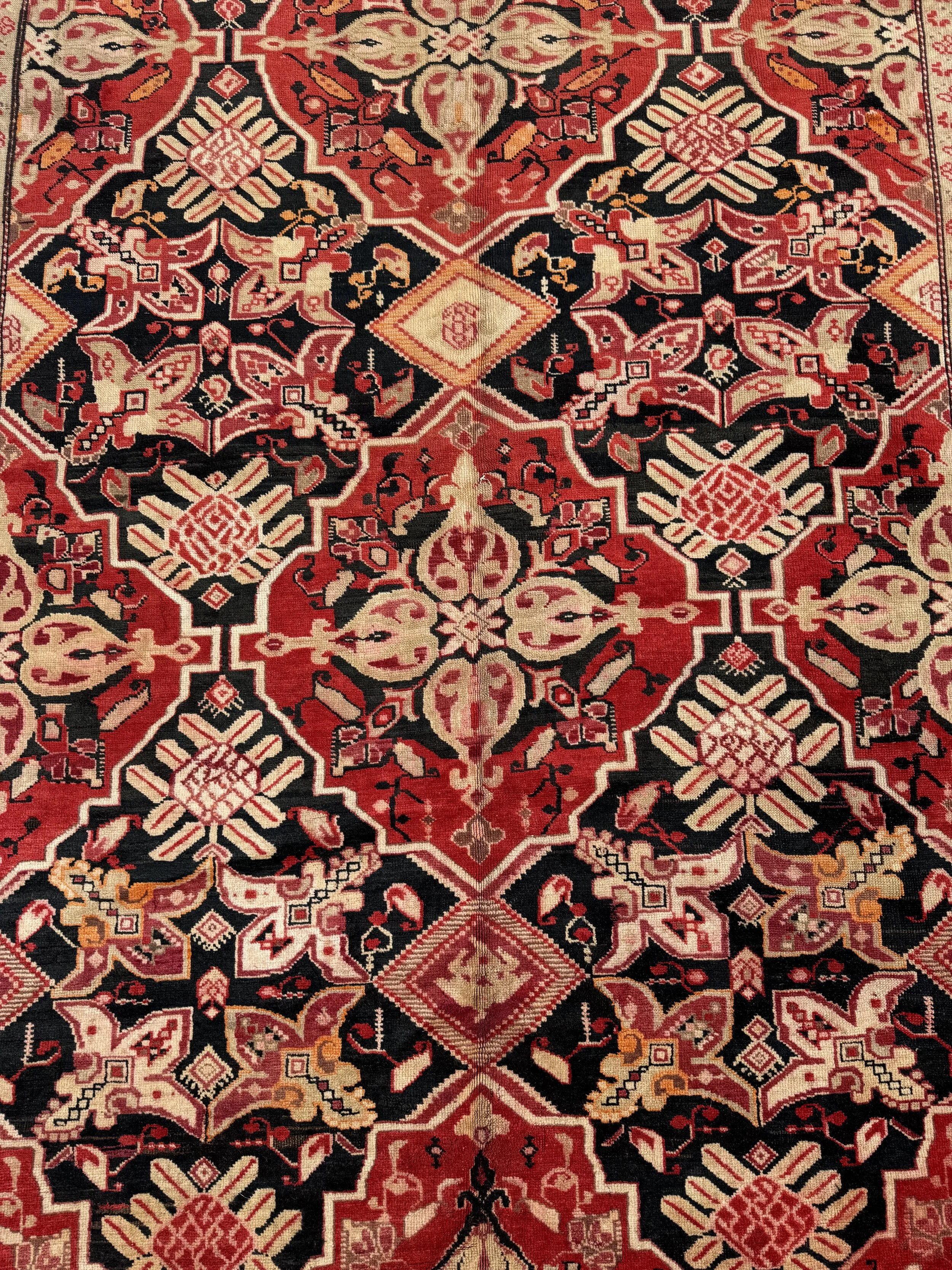Close-up view of a traditional Persian-style area rug with intricate geometric and floral patterns in red, black, beige, and hints of orange.
