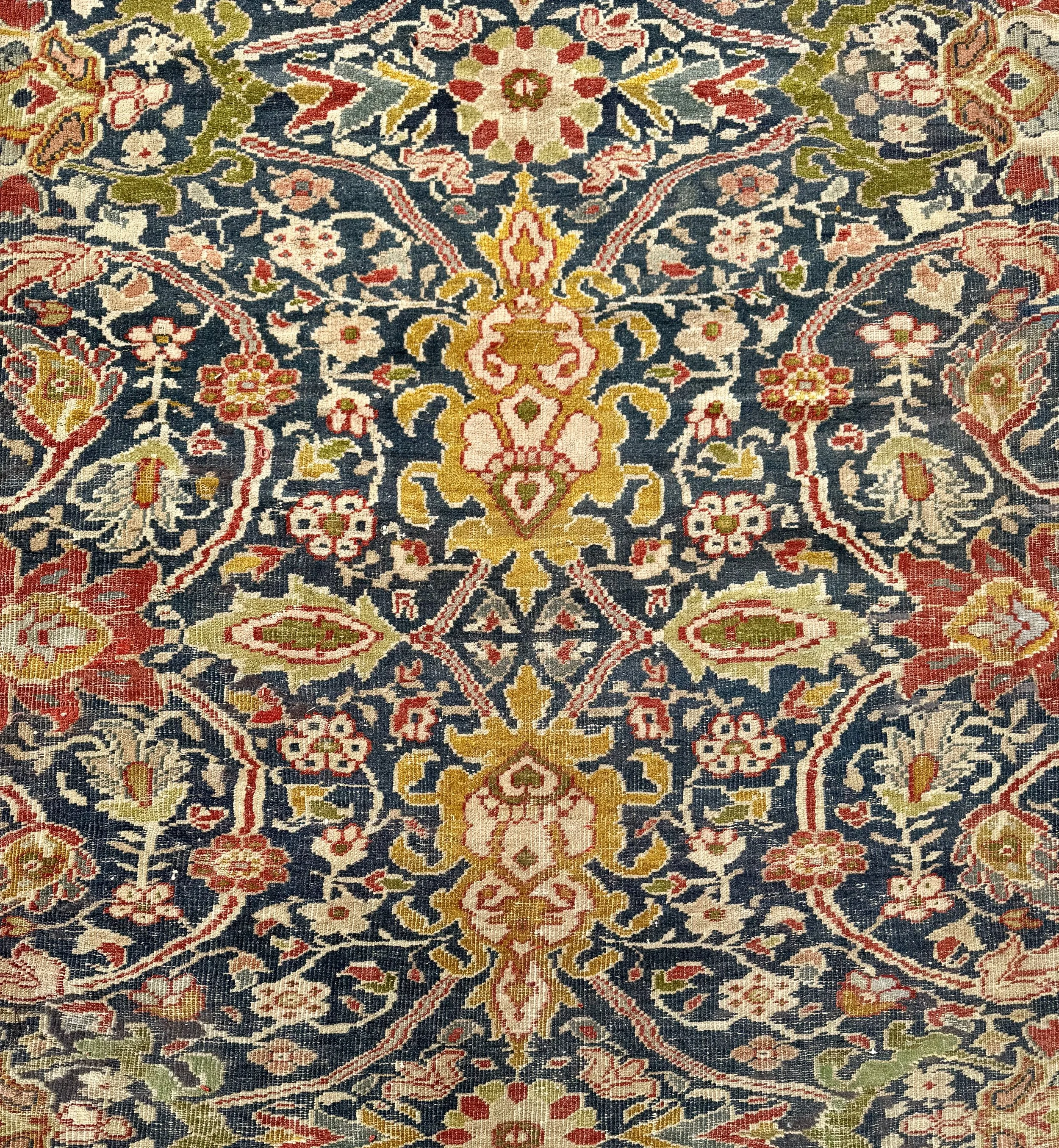 Close-up of an intricately patterned traditional woven rug with floral and geometric motifs in shades of red, pink, yellow, green, and navy blue.