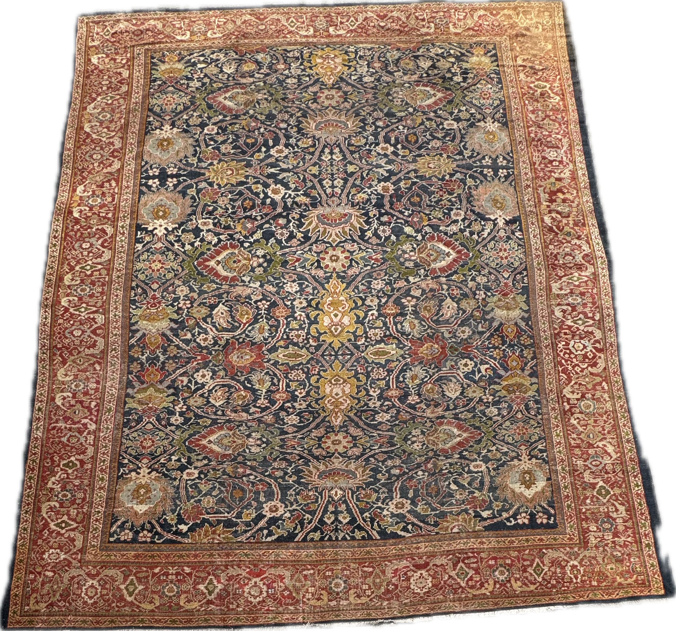 A vintage oriental area rug with a navy background, floral and vine motifs in gold, red, green, and beige, surrounded by a red and beige decorative border.