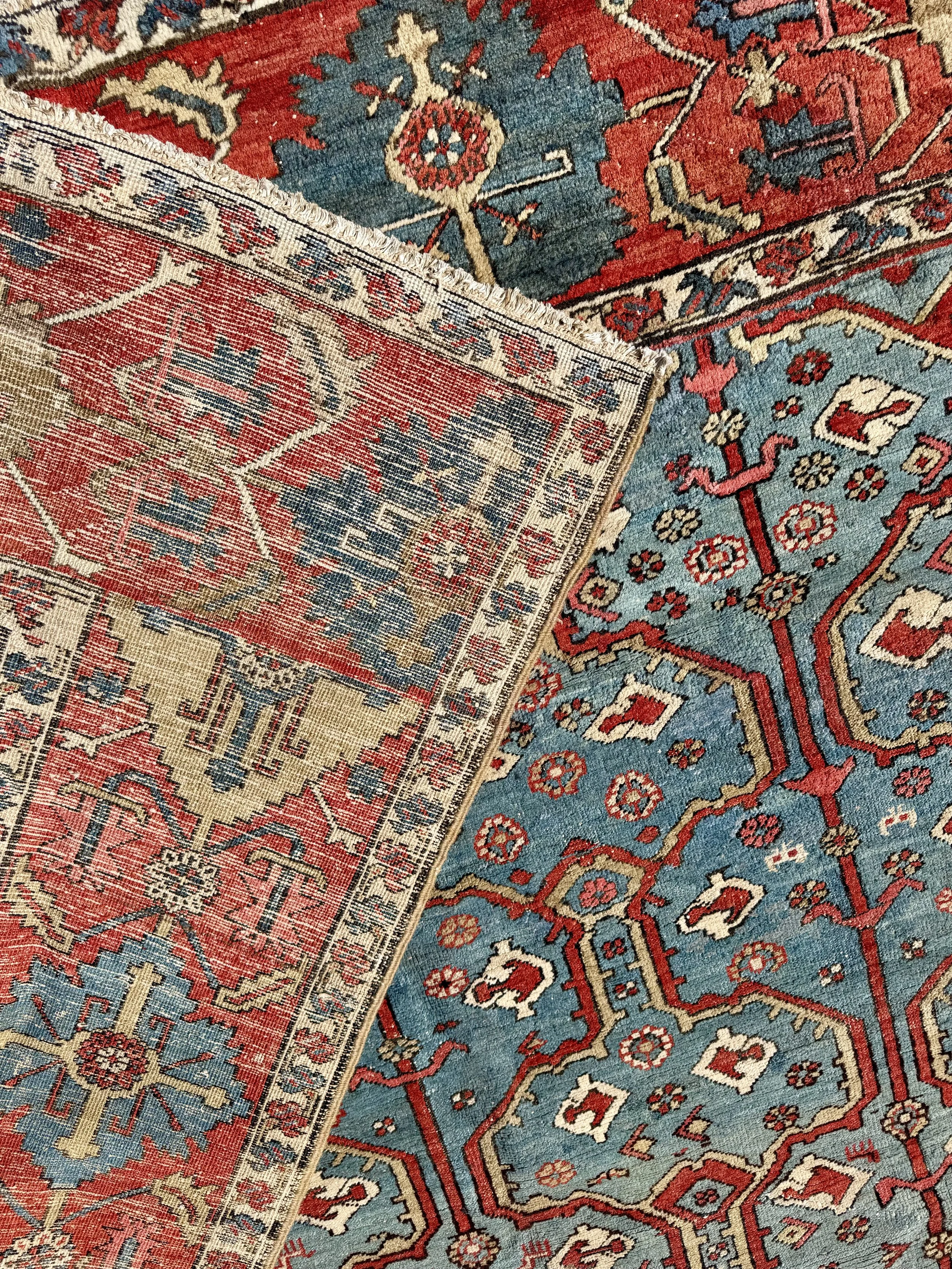 Close-up of two overlapping Persian rugs with intricate floral and geometric patterns in red, blue, beige, and cream colors.