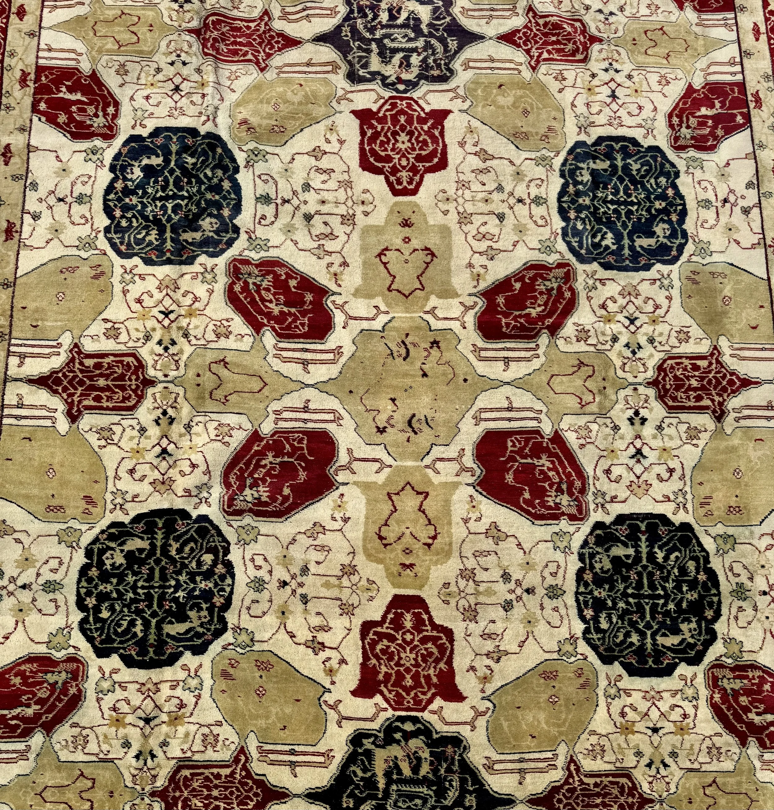 A patterned area rug with intricate geometric and floral designs in red, beige, black, and green colors.