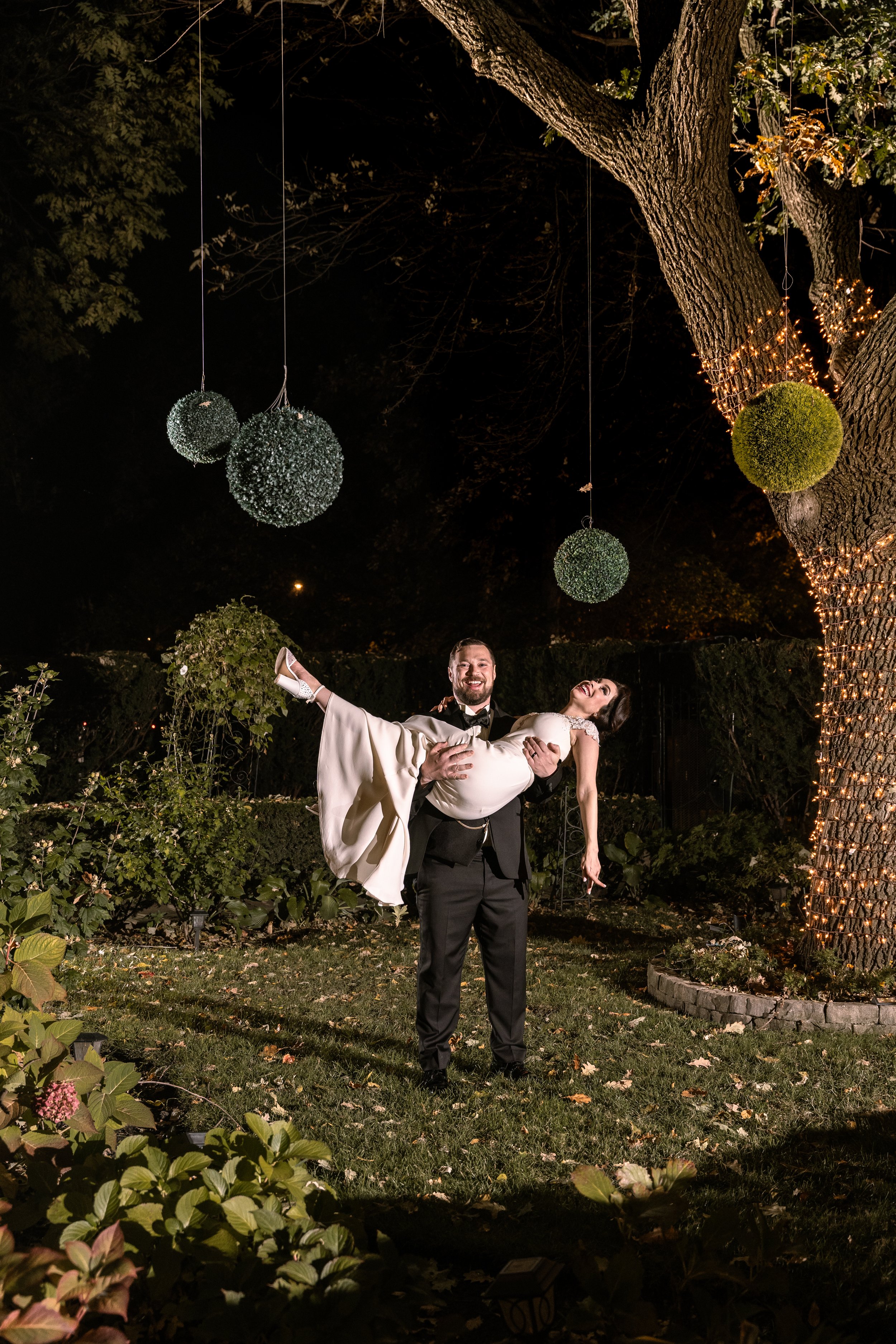 A groom carries his Bride at night in a garden of a Chicago Wedding Venue.