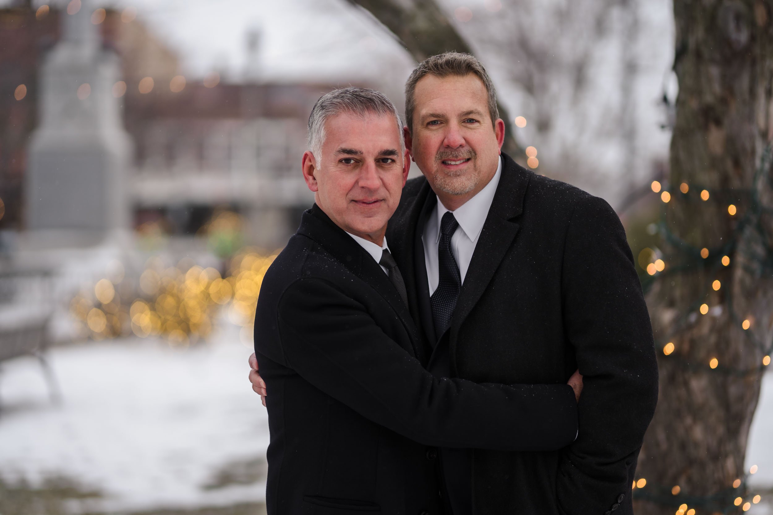 Two grooms cozy up in the snow during their winter elopement in Woodstock, IL.