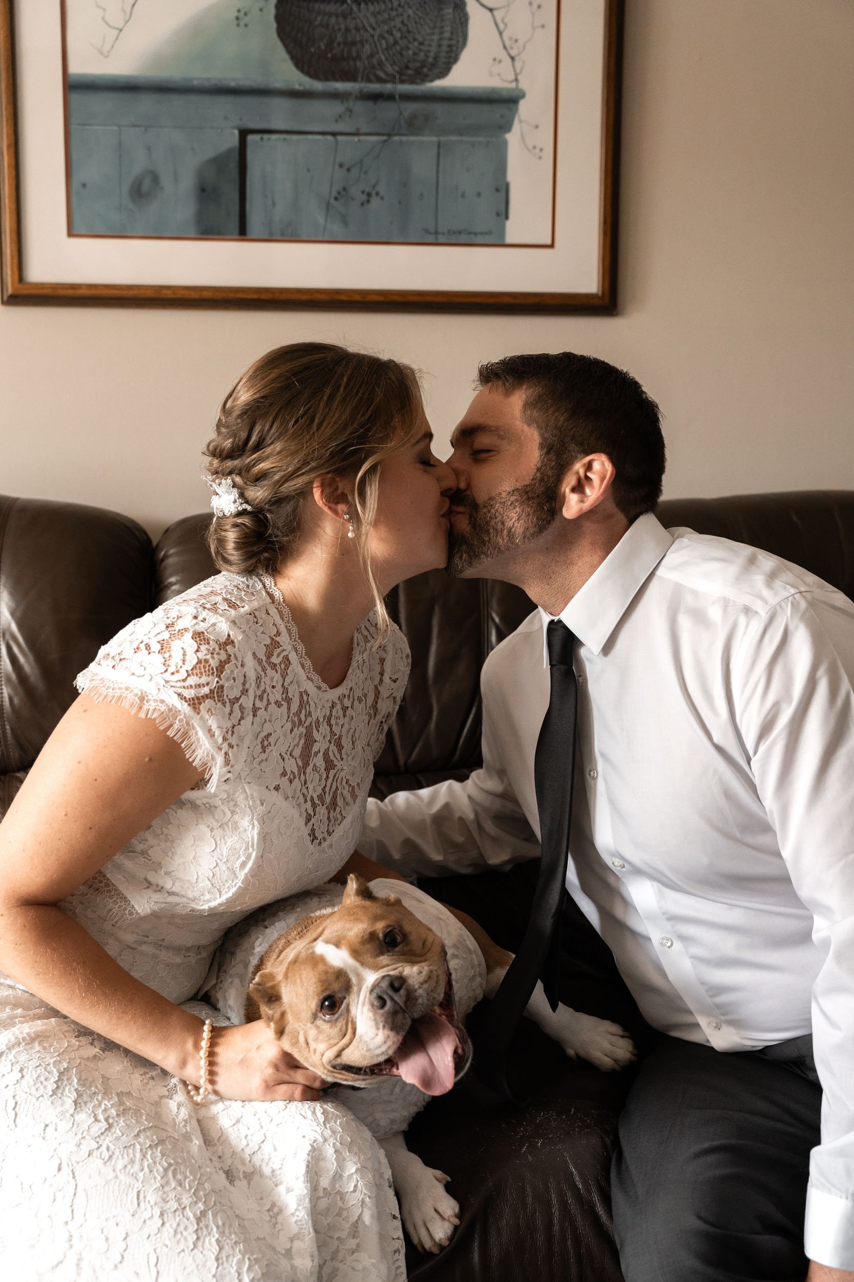 A couple kisses while snuggling with their pup just after their Backyard Wedding Ceremony in Barrington, IL.