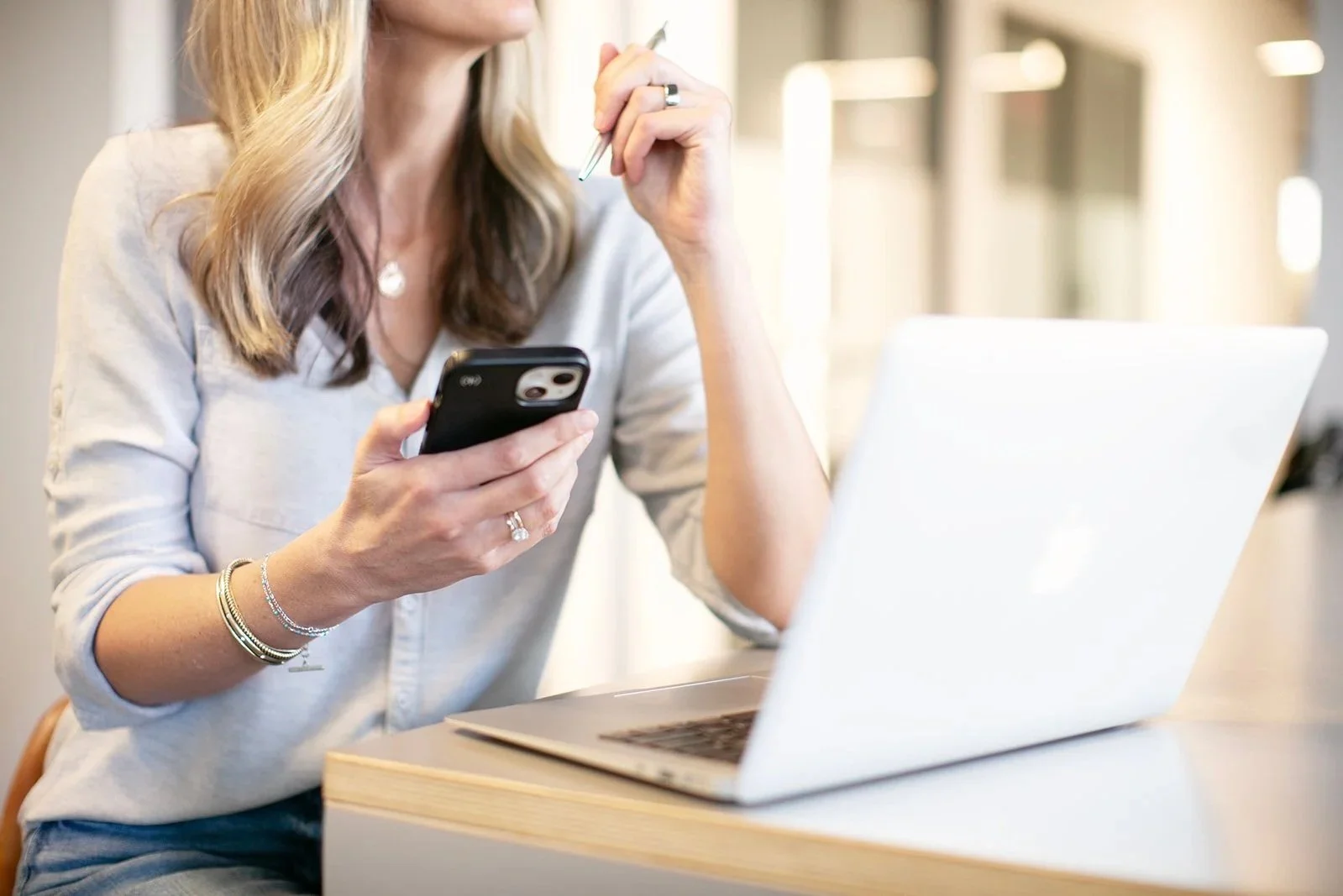 Woman with a laptop, phone, and coffee at a bright workspace