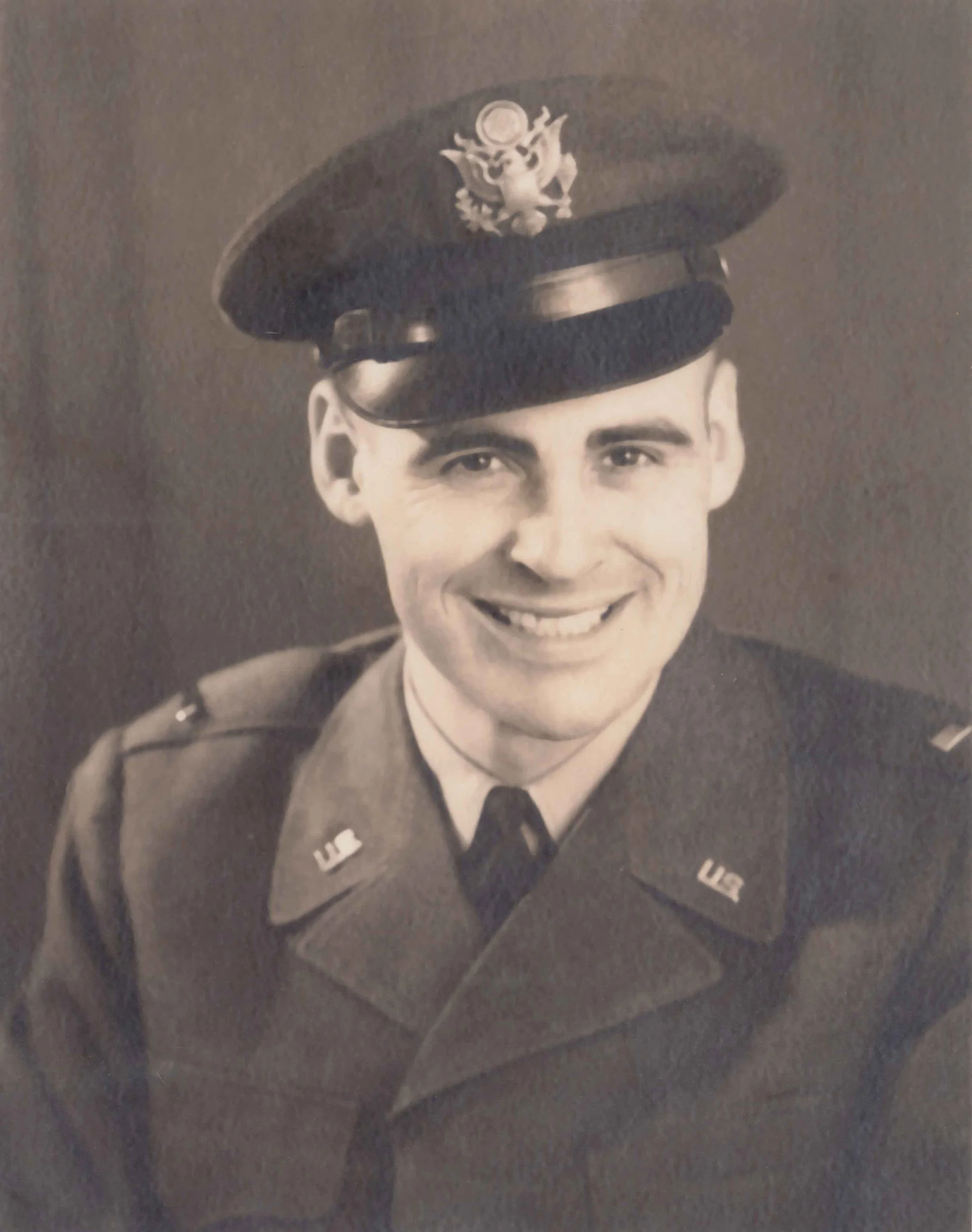 Black and white portrait of a smiling young military officer in uniform, wearing a peaked cap with an insignia.
