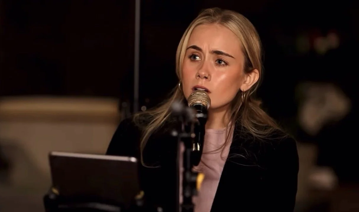 Young woman singing into a microphone in a dimly lit room.