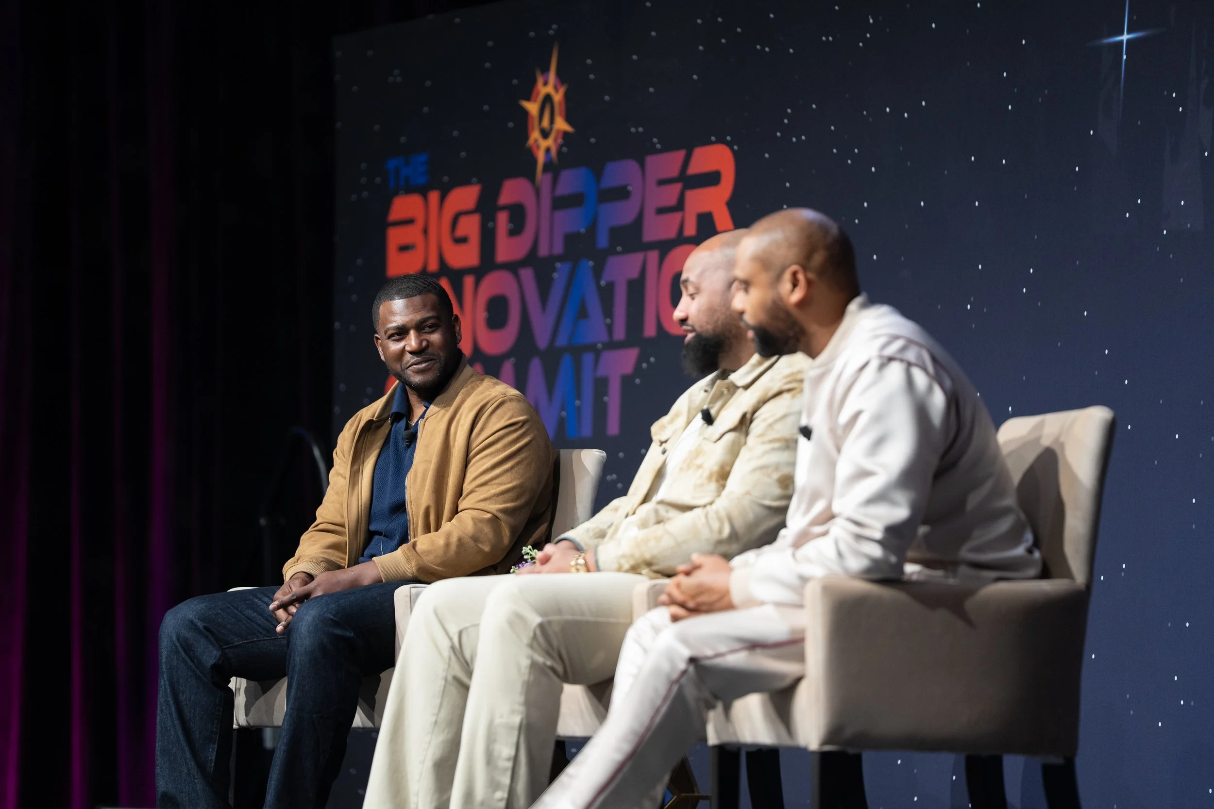 Three men sitting on stage chairs during a panel discussion at the Big Dipper Innovation Summit, with a backdrop displaying the event logo.
