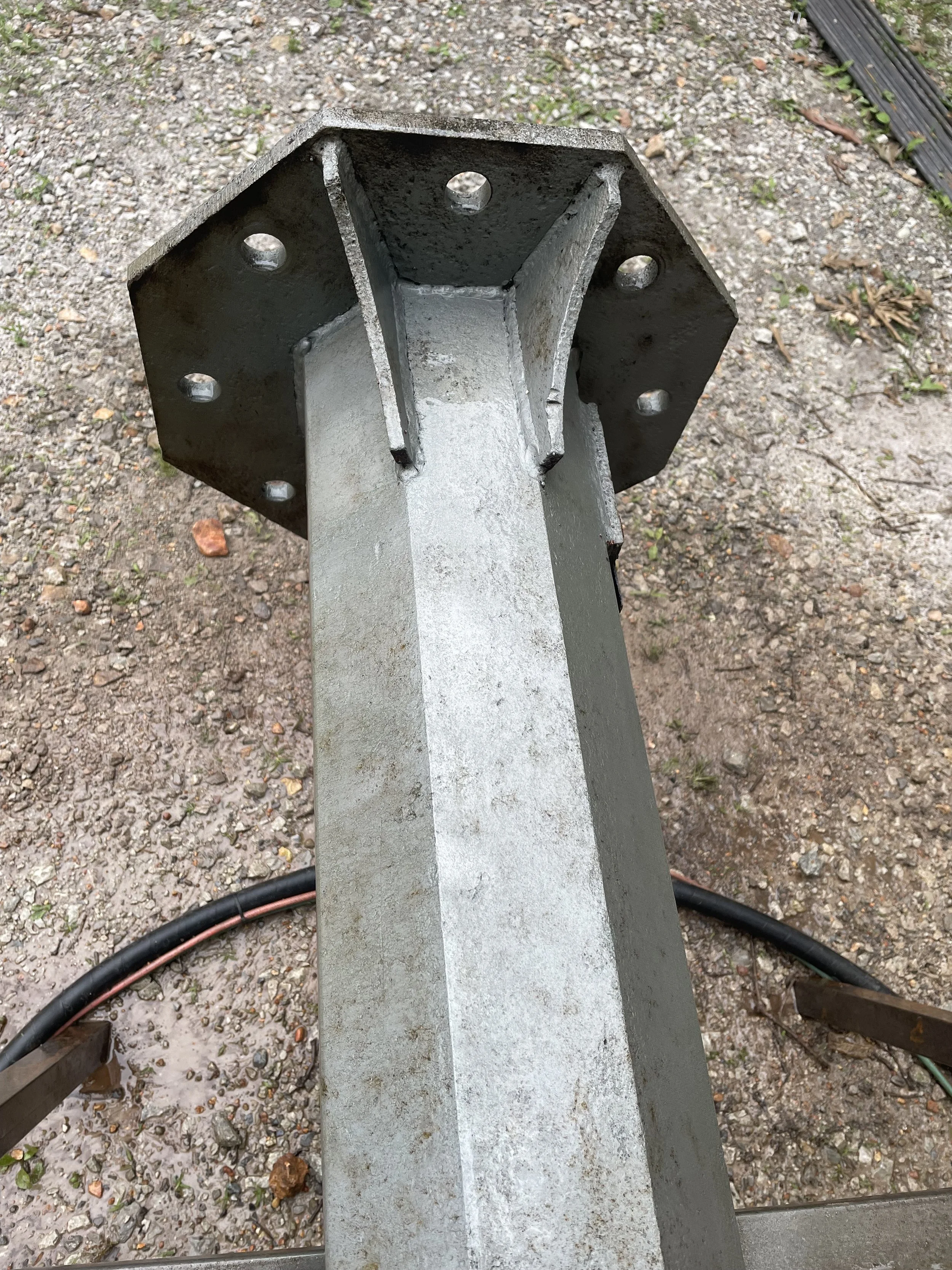 Close-up view of a metal support beam with a flanged end, on a gravel ground outdoors.