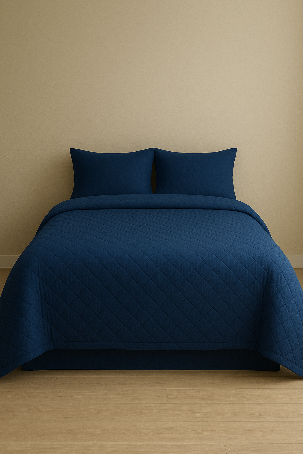 Cama con colcha y almohadas de color azul oscuro, en una habitación con pared beige y suelo de madera.