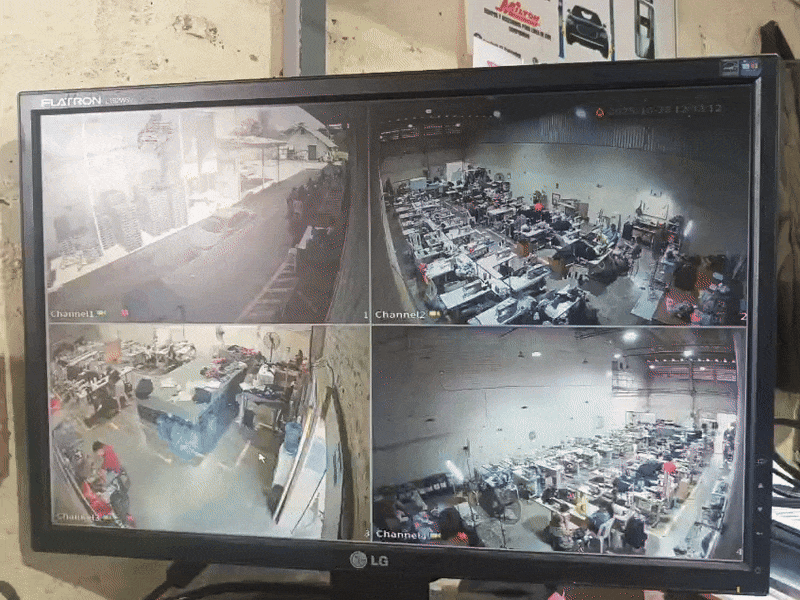 Monitor de seguridad con cuatro cámaras en una sala de trabajo y en un estacionamiento, mostrando distintas áreas con personas y vehículos.