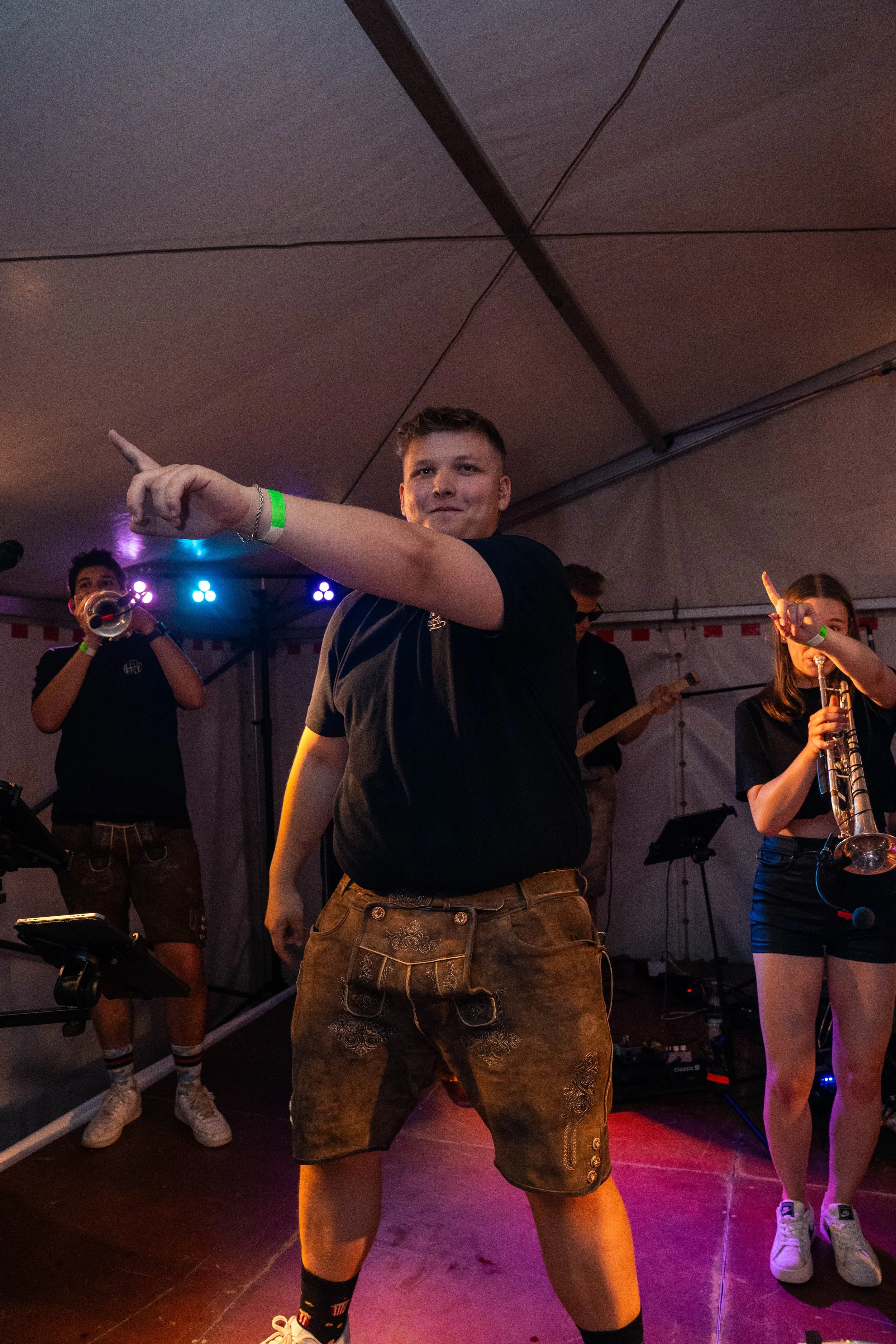 Junge Männer und Frauen in einer Musikband beim Auftritt in einem Zelt, singend und musizierend, mit bunten Lichter im Hintergrund.