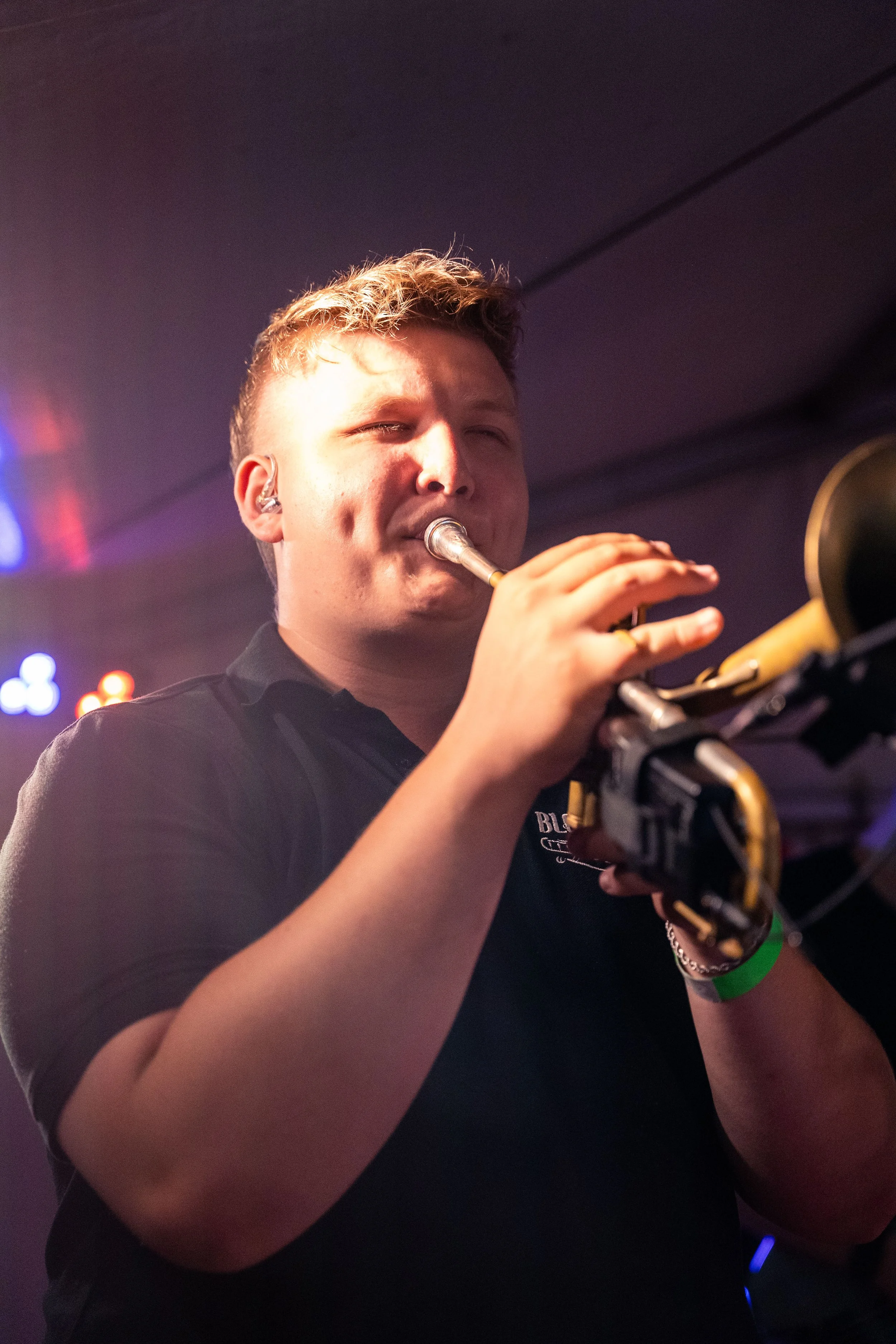 Mann spielt Trompete bei einem Konzert, dunkler Hintergrund mit bunten Lichtern.