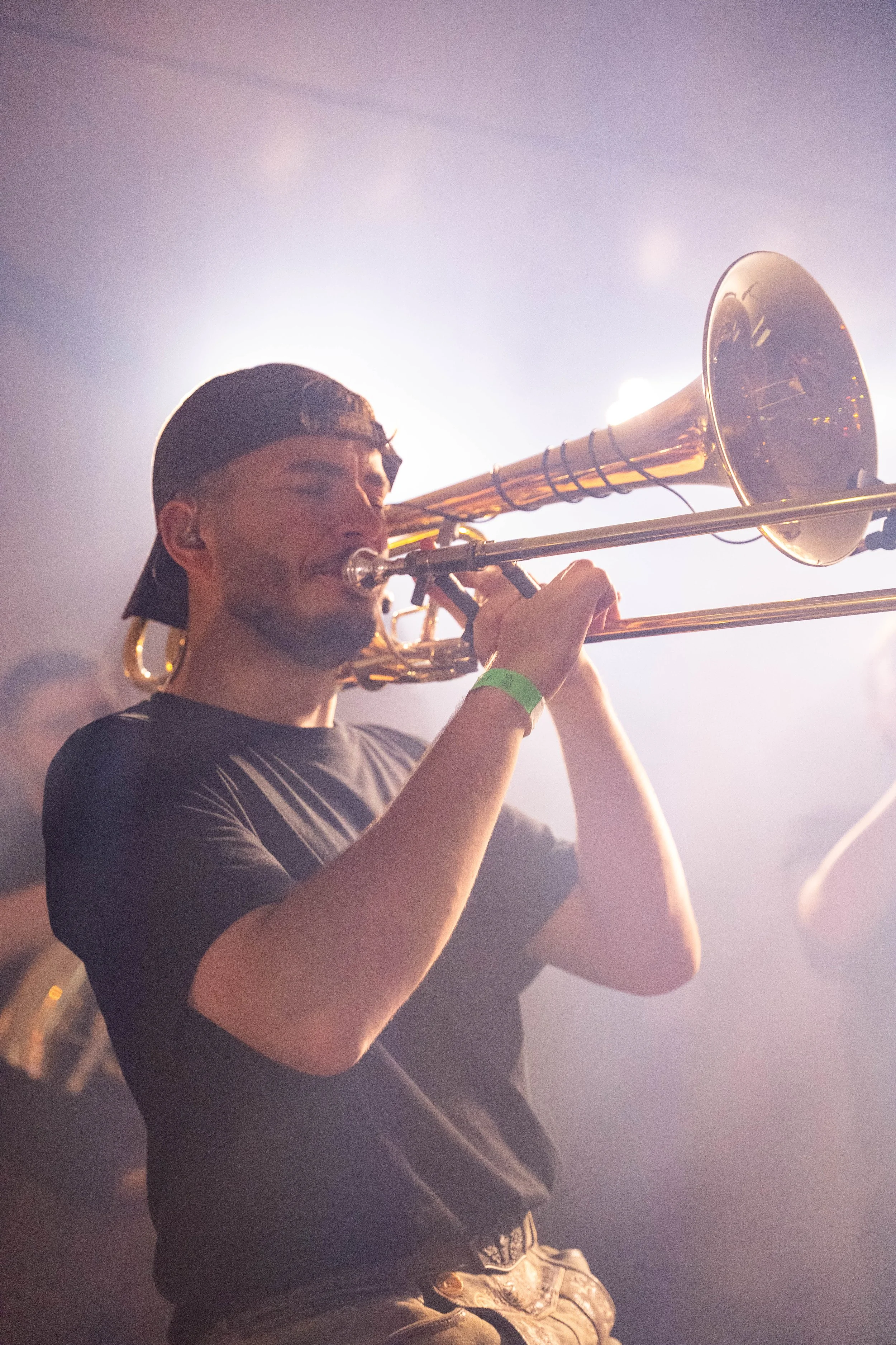 Männlicher Musiker spielt  Posaune bei einem Live-Auftritt, mit diffusem Licht im Hintergrund.